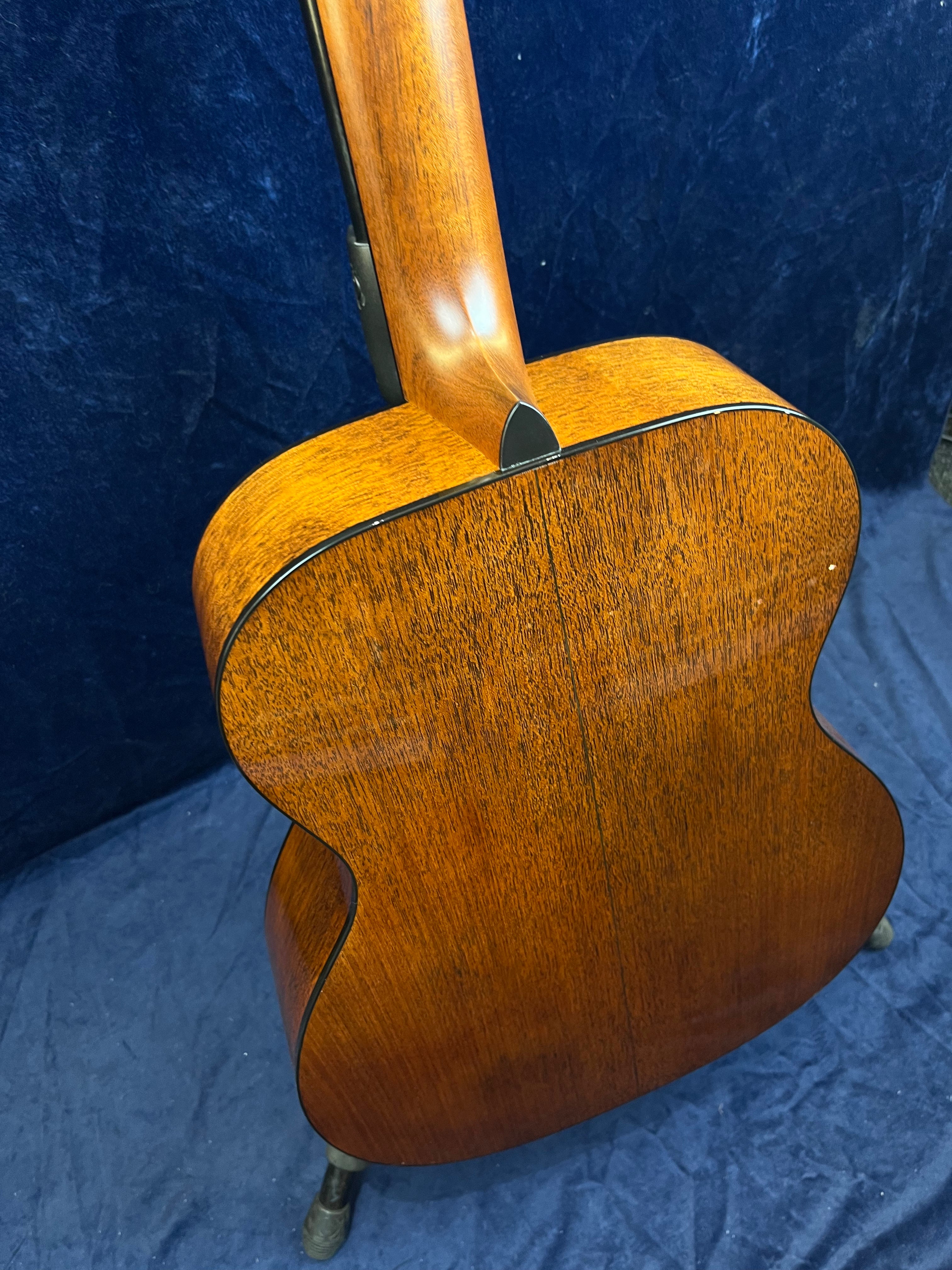 The back and neck of an acoustic guitar made of warm, rich brown wood with a visible grain pattern and a glossy finish.