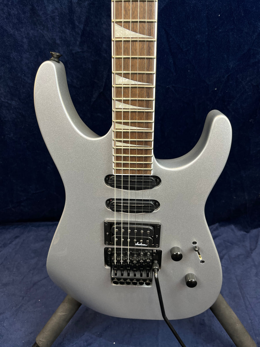 Guitare électrique gris métallisé avec trois micros, deux boutons noirs, un sélecteur et vibrato Floyd Rose, manche à repères triangulaires.