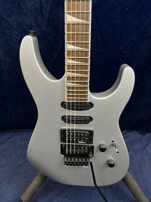 Silver electric guitar with three pickups, a Floyd Rose tremolo bridge, two control knobs, a selector switch, and triangular fretboard inlays.