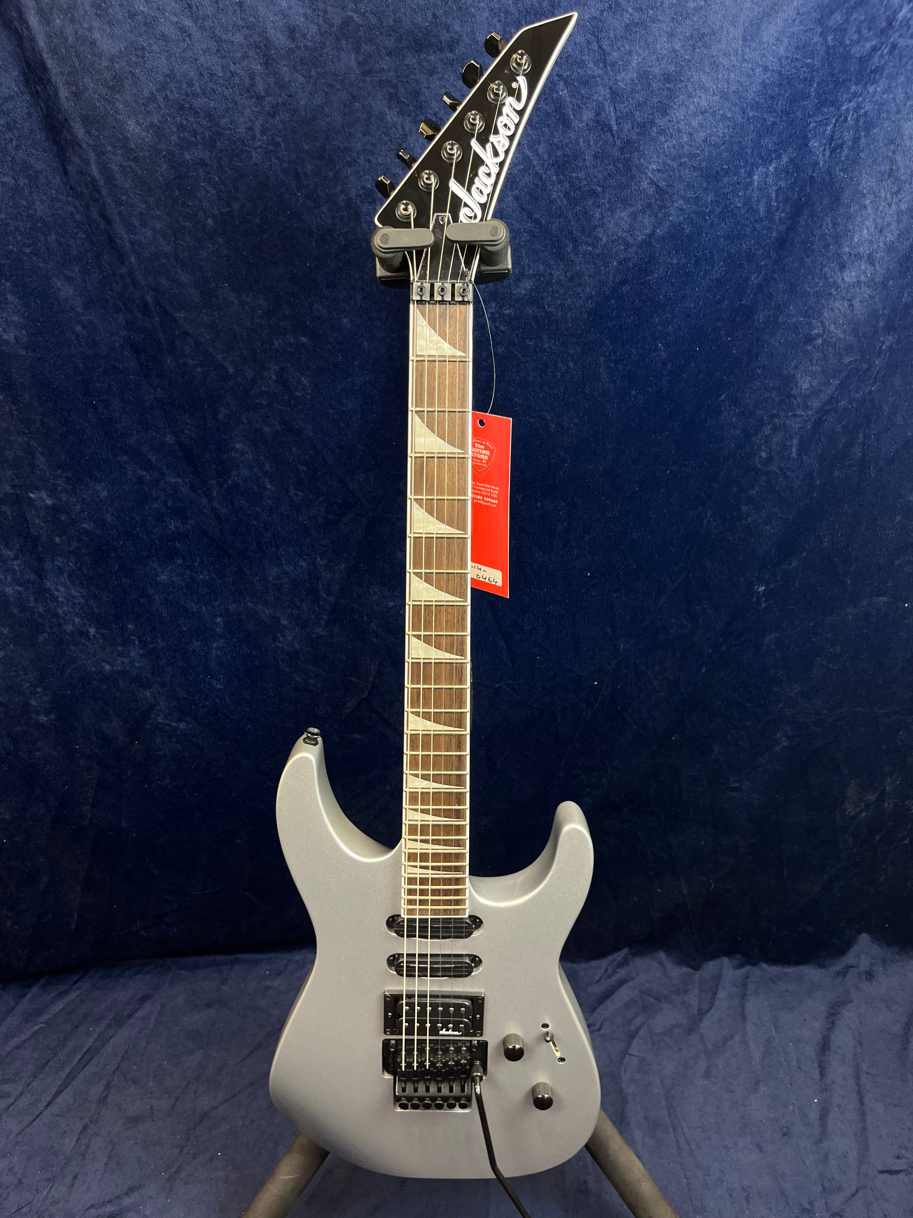 Guitare électrique Jackson gris métal à double pan coupé, manche orné d'incrustations en V, trois micros noirs, chevalet Floyd Rose.