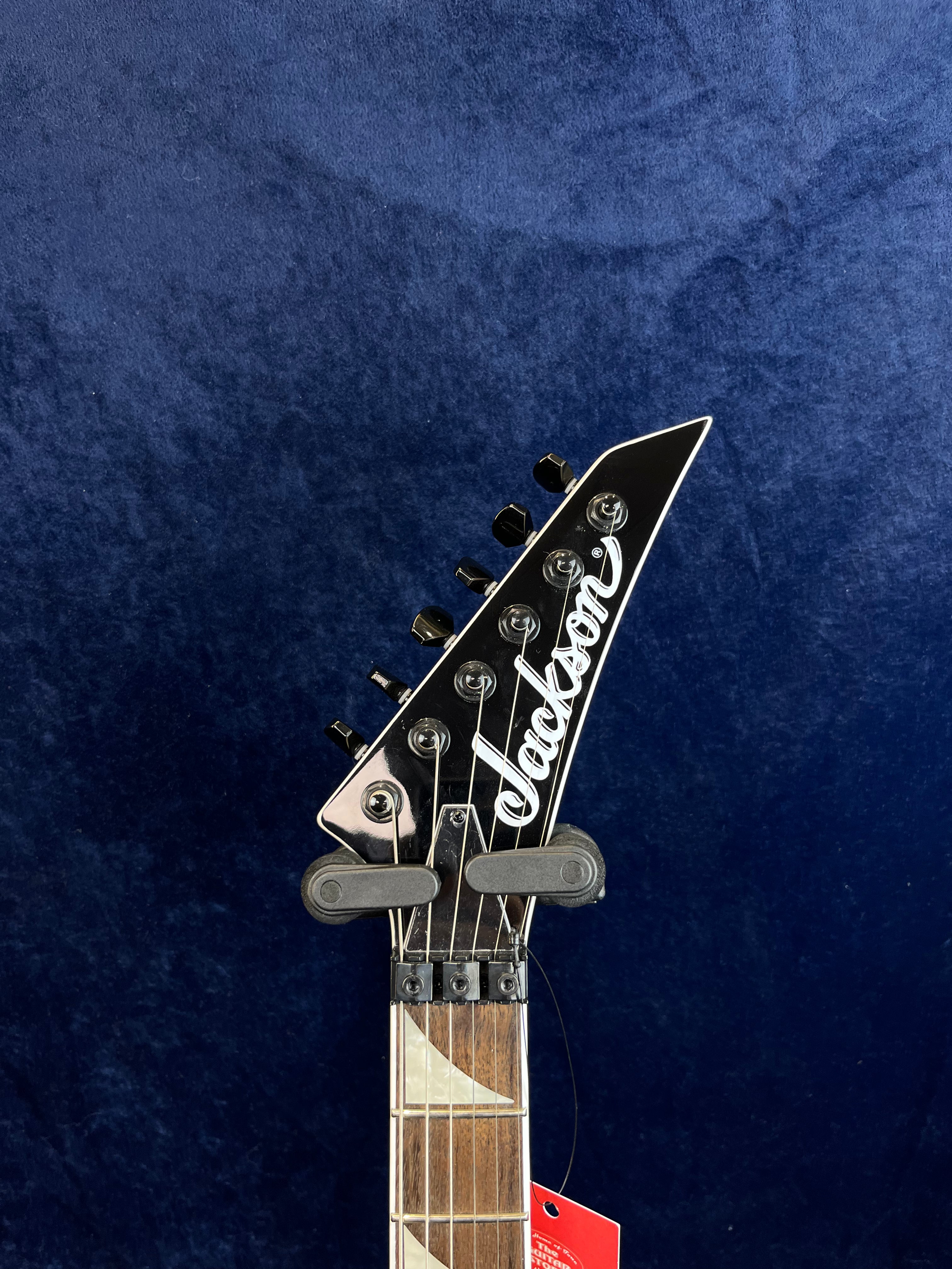 Gros plan sur la tête noire pointue d’une guitare électrique Jackson, avec six mécaniques noires alignées et un sillet à blocage.