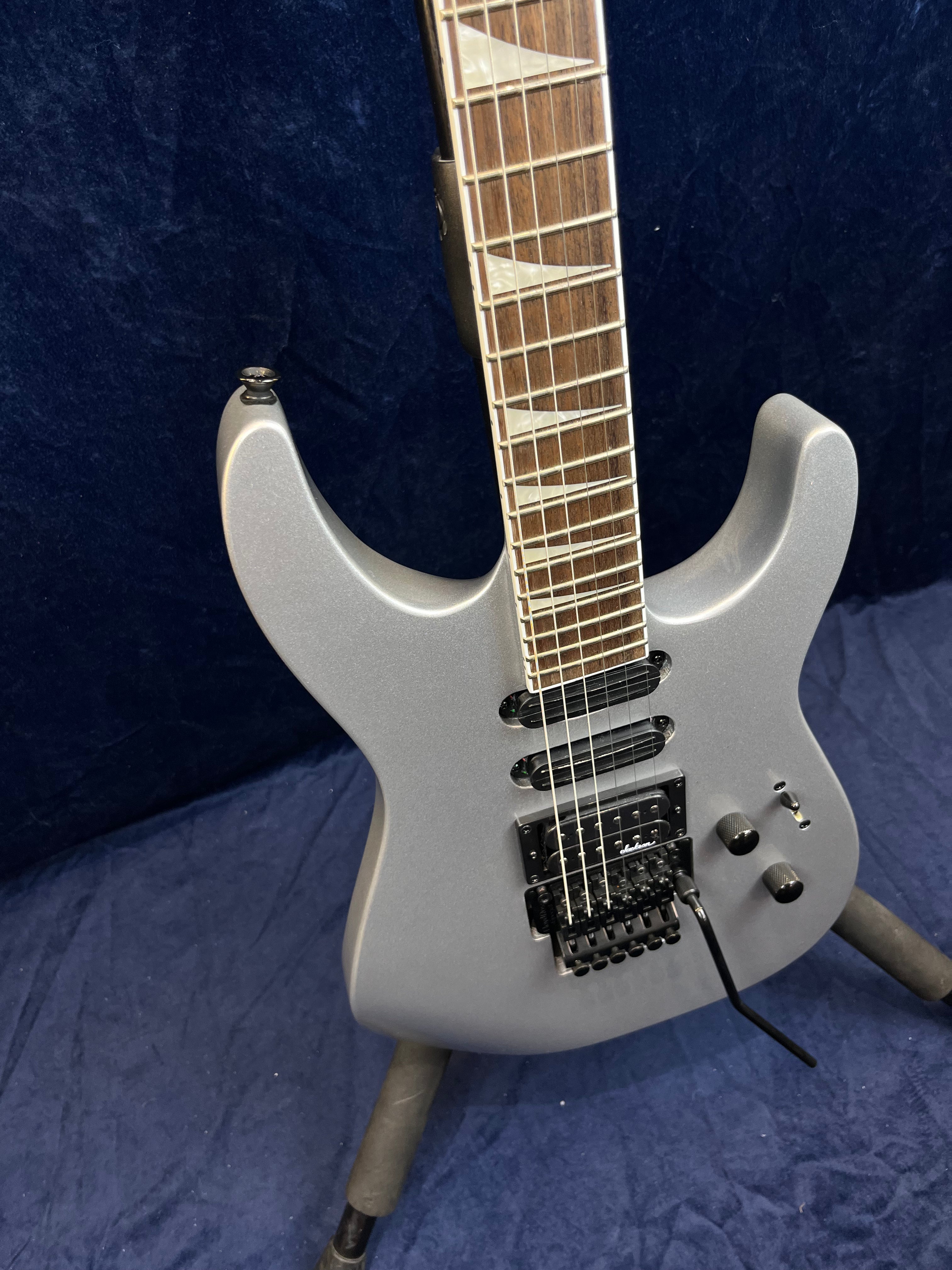 Guitare électrique gris mat avec trois micros noirs, vibrato Floyd Rose et repères triangulaires blancs sur la touche en bois brun.