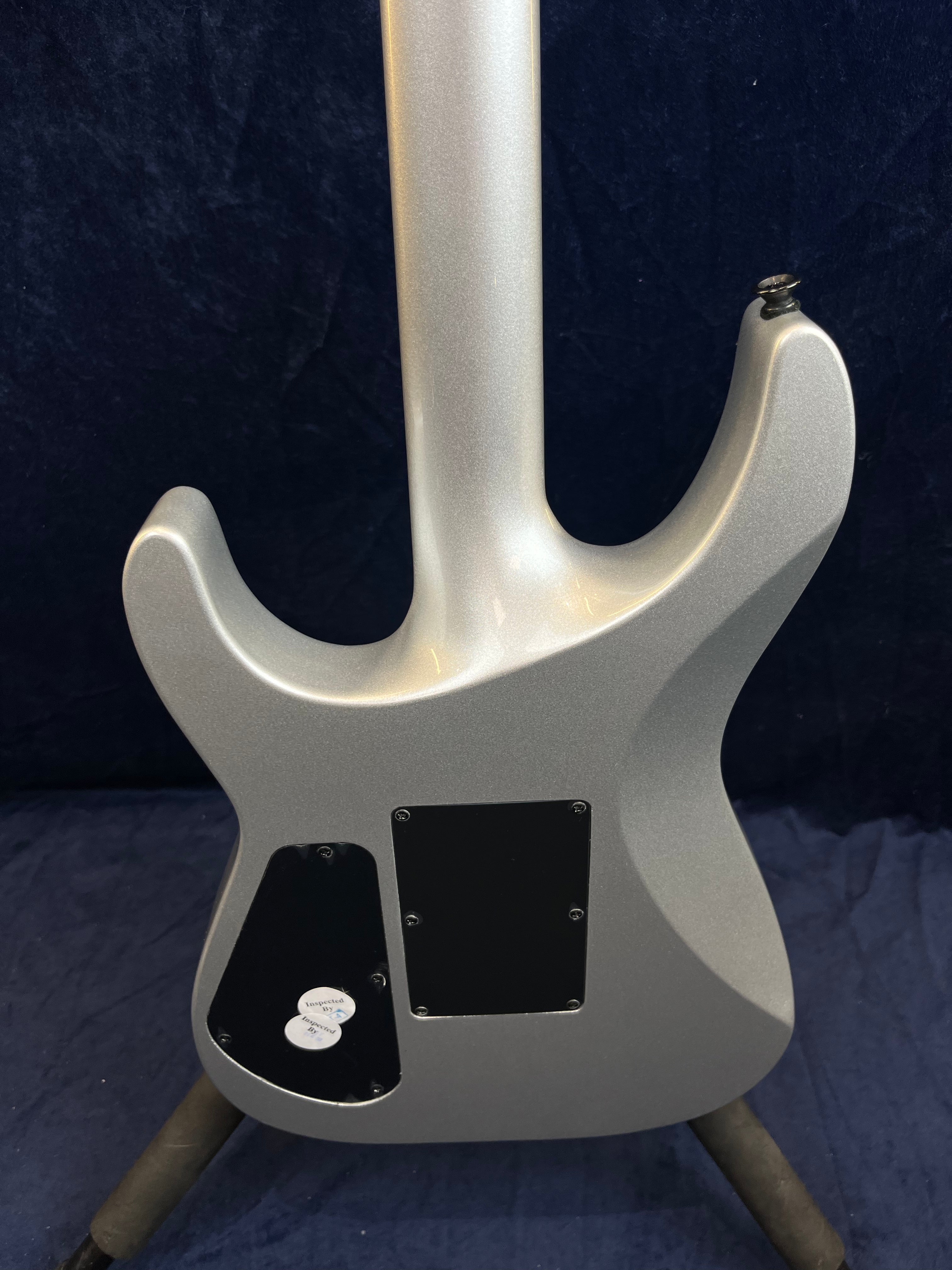 Guitare électrique gris métallisé vue de dos, avec deux plaques d’accès noires et stickers d’inspection dans un coin.