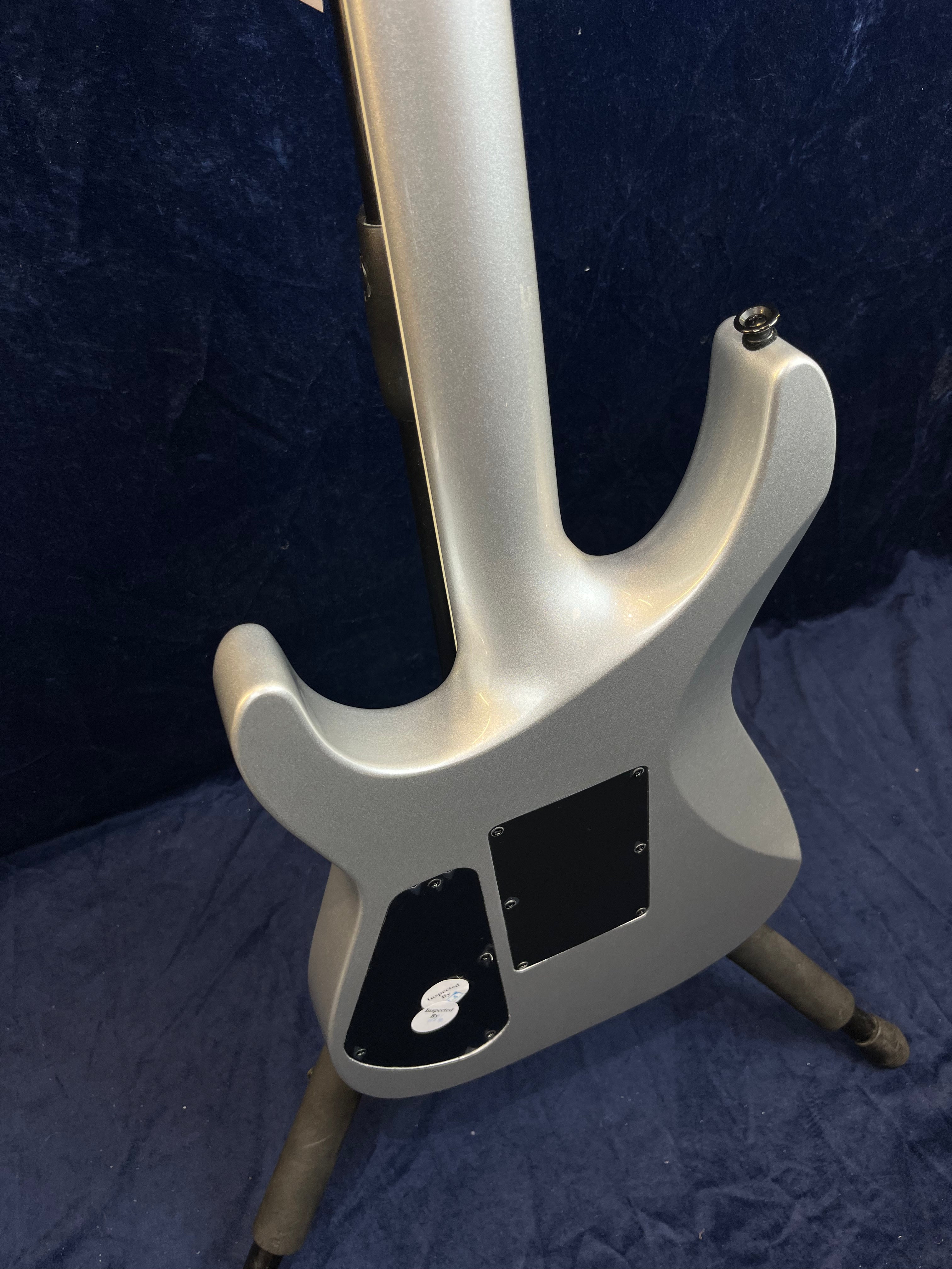 Guitare électrique gris métallisé vue de dos, deux plaques d’accès noires vissées sur le corps, posée sur un support noir.