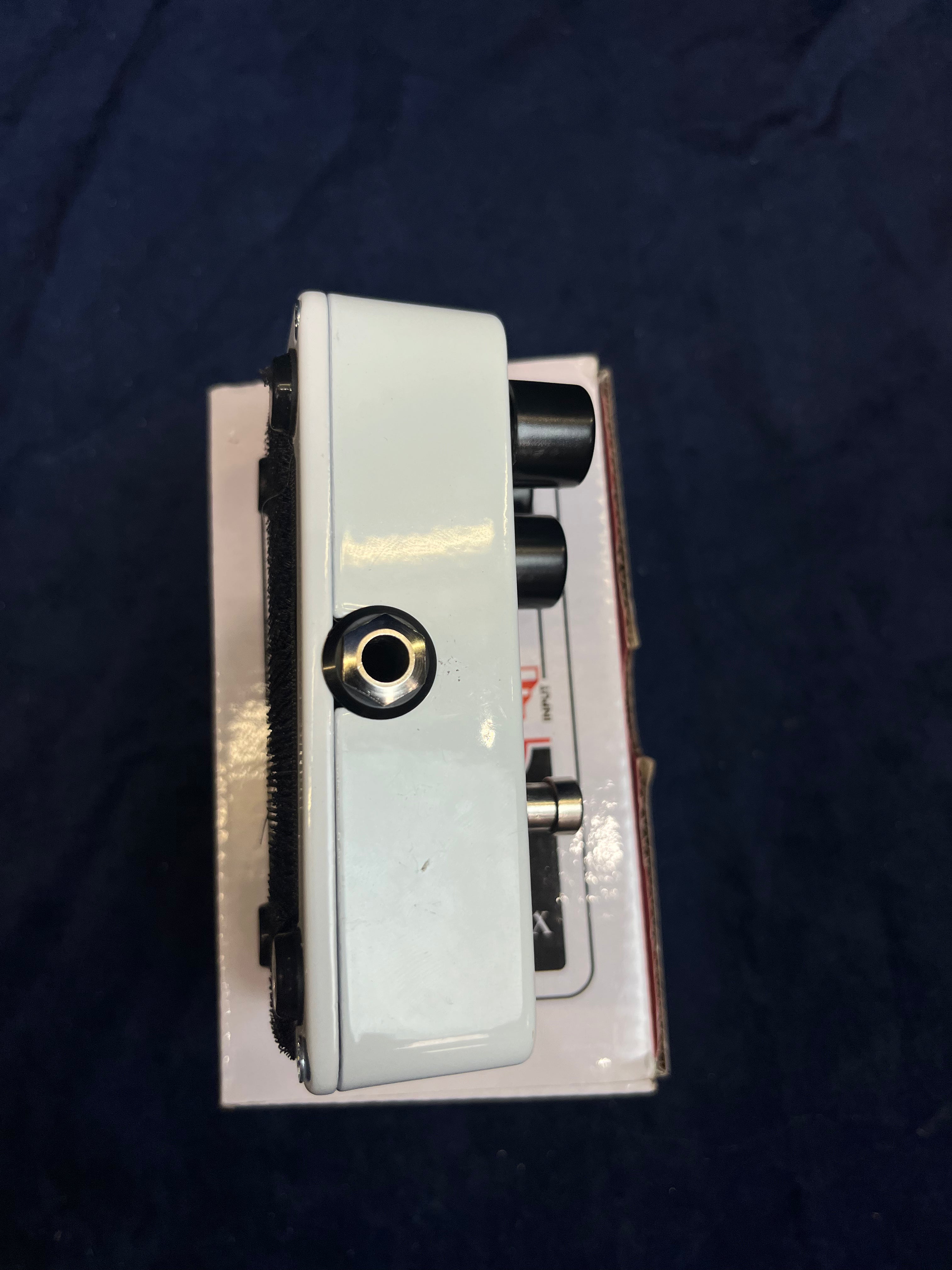 White FX pedal seen from the side, showing a single input jack, three black control knobs, and a metal footswitch on top.