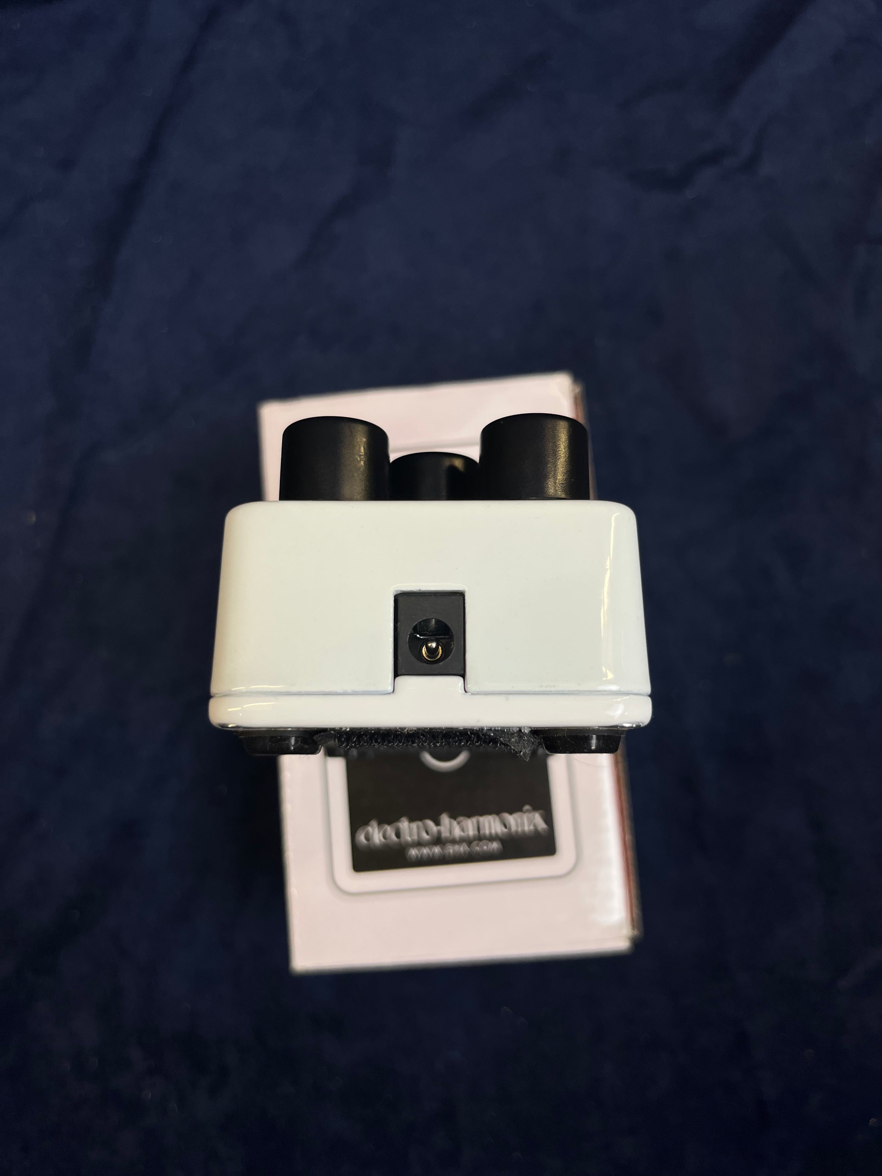 White FX pedal viewed from the top edge with two black knobs and a central power input jack, placed on an Electro-Harmonix branded box.