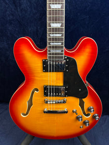 Sunburst semi-hollow electric guitar with double cutaways, two humbucker pickups, f-holes, black pickguard, and four control knobs.