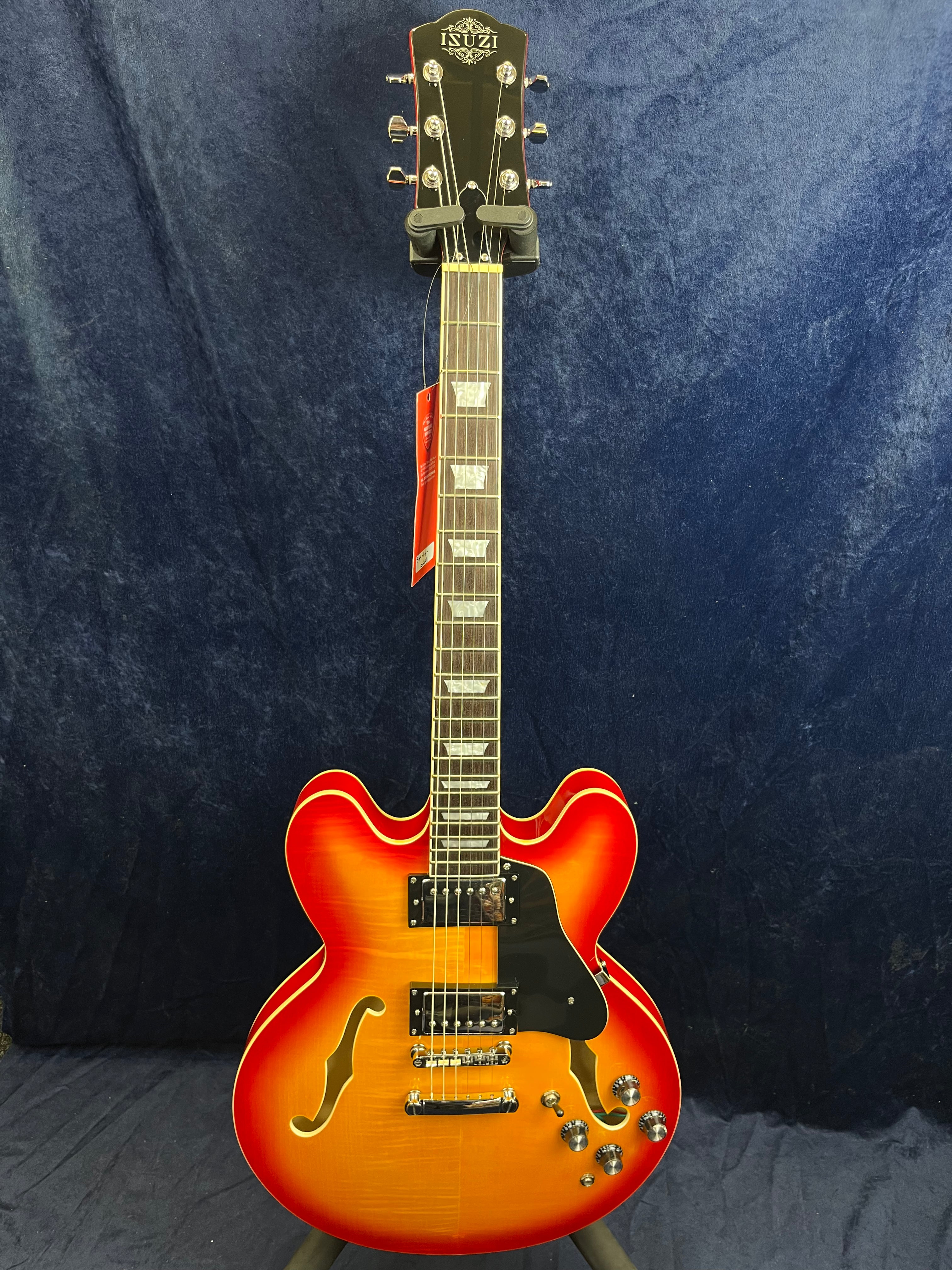 Sunburst semi-hollow electric guitar with two humbucker pickups, four control knobs, black pickguard, f-holes, and ISUZI logo on the headstock.