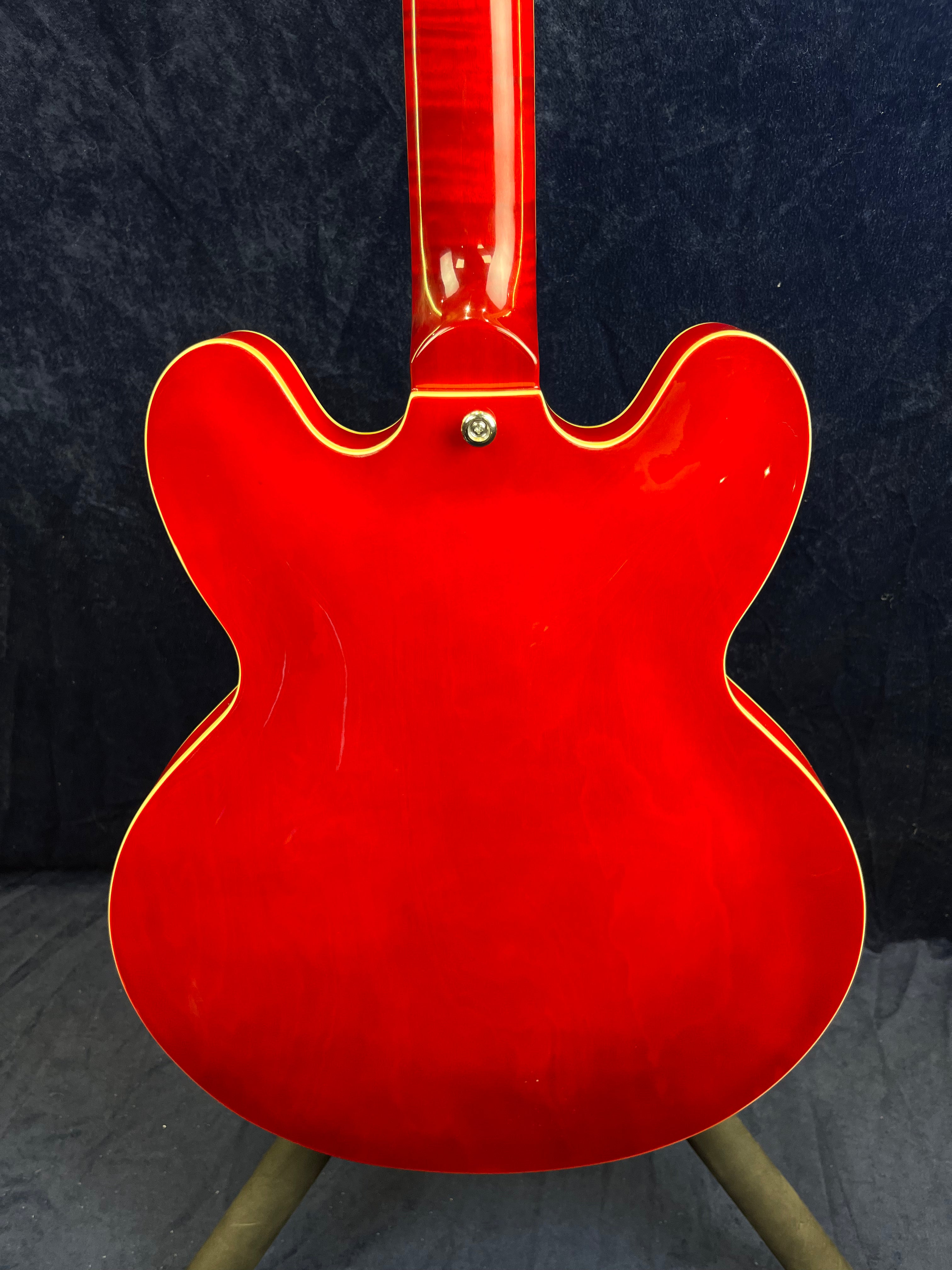 Bright red semi-hollow electric guitar shown from the back, with cream binding outlining its double-cutaway body and neck.