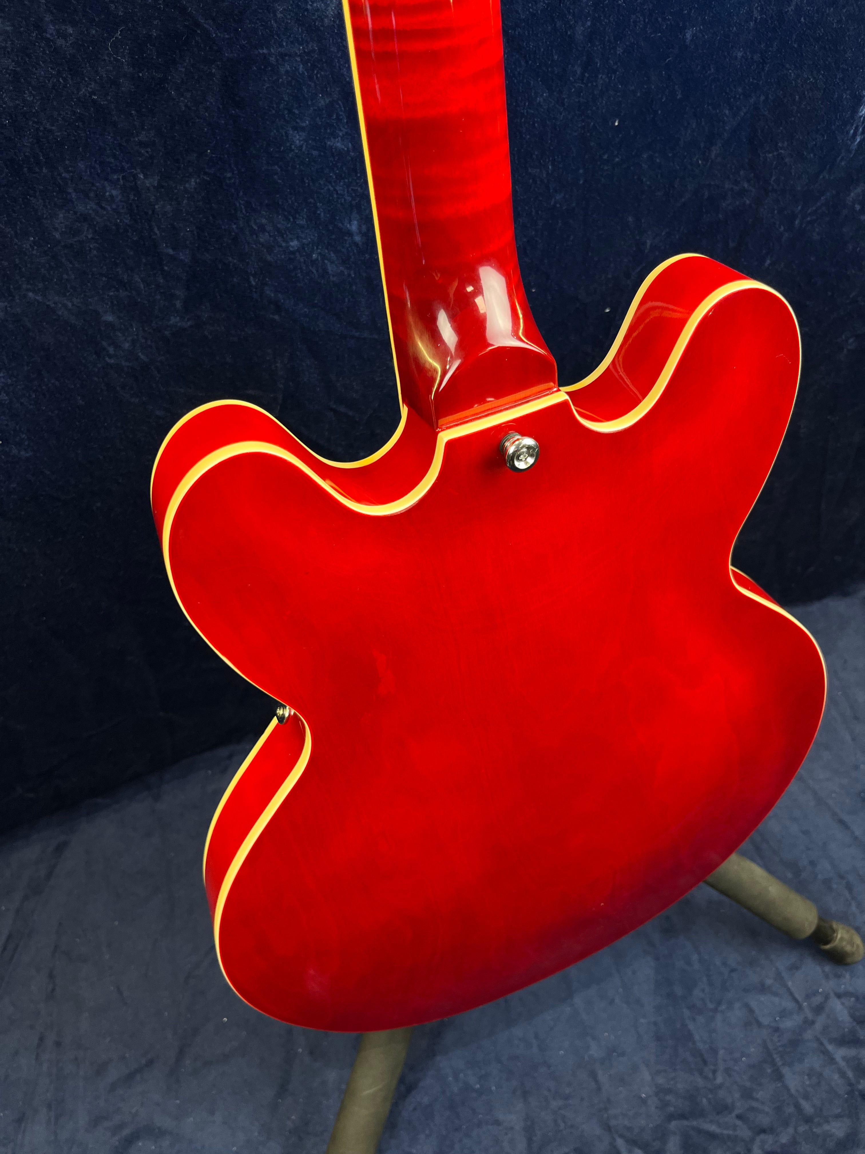 Electric guitar with a glossy cherry red finish, yellow binding along the edges, and a semi-hollow double cutaway body style seen from the back.