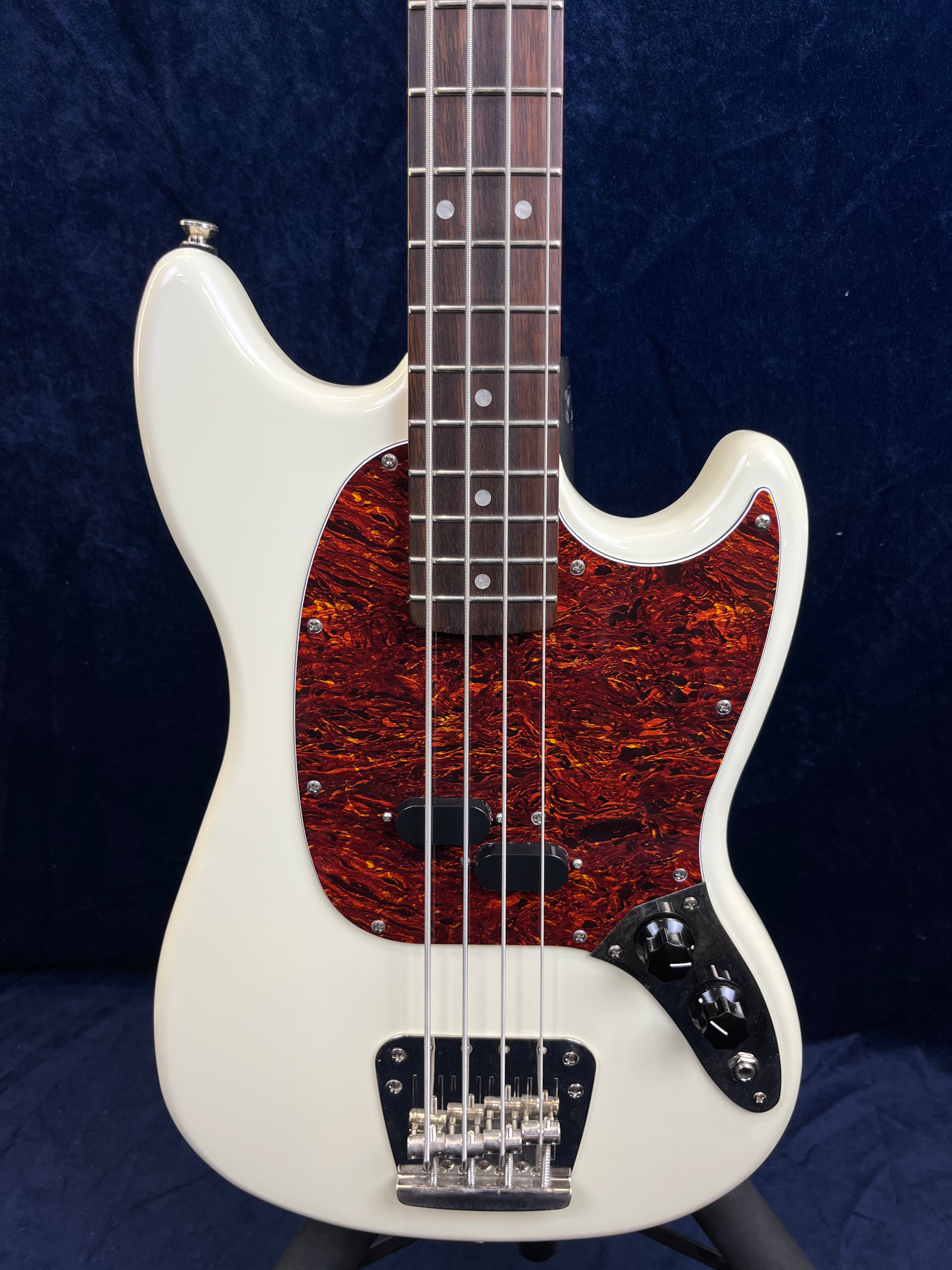 White bass guitar with four strings, a dark red tortoiseshell-style pickguard, chrome bridge, and two black control knobs on a metallic plate.