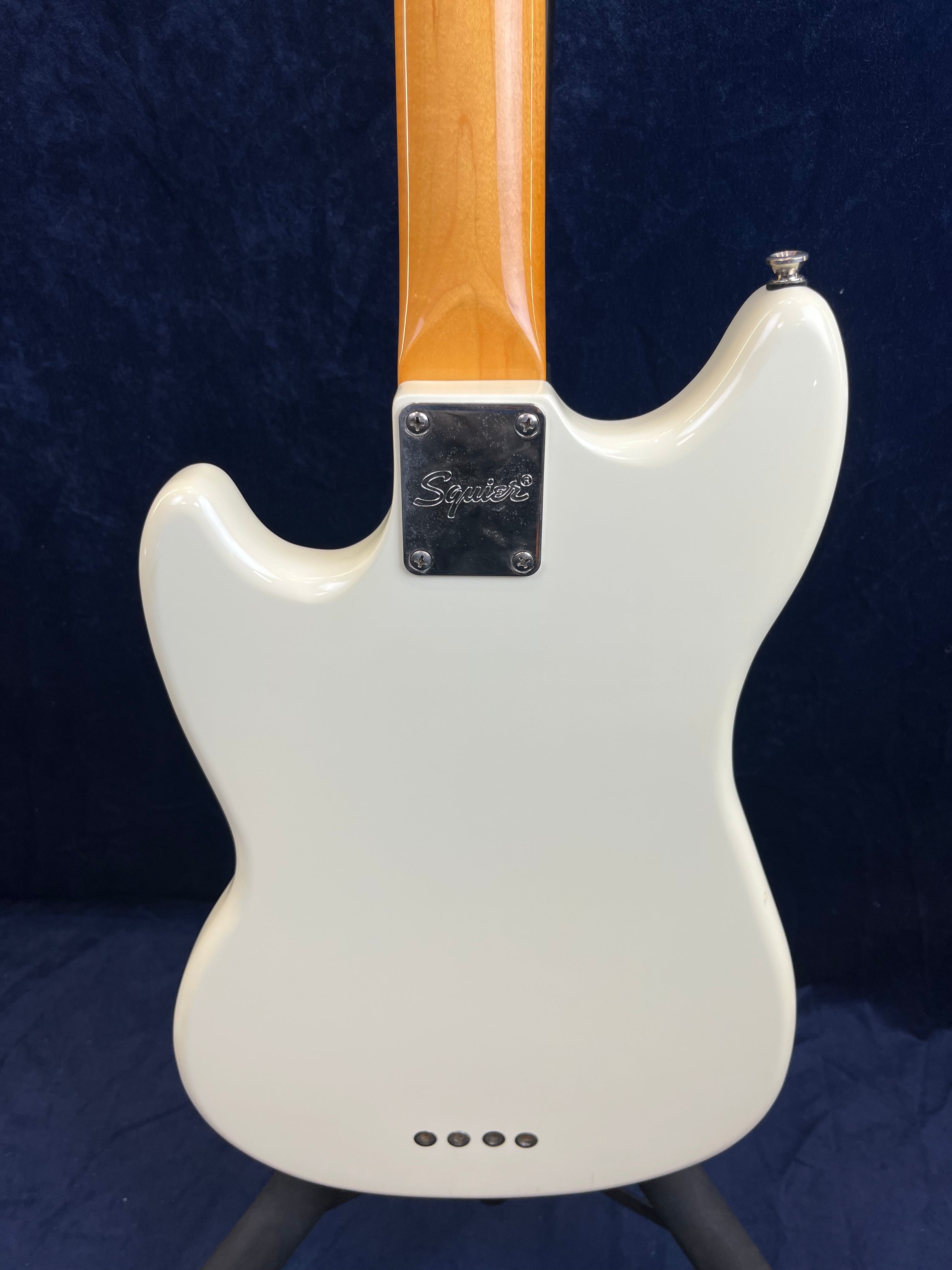 Back of a white Squier bass guitar showing the neck joint with a metal plate and four screws, plus a row of string ferrules near the bottom.