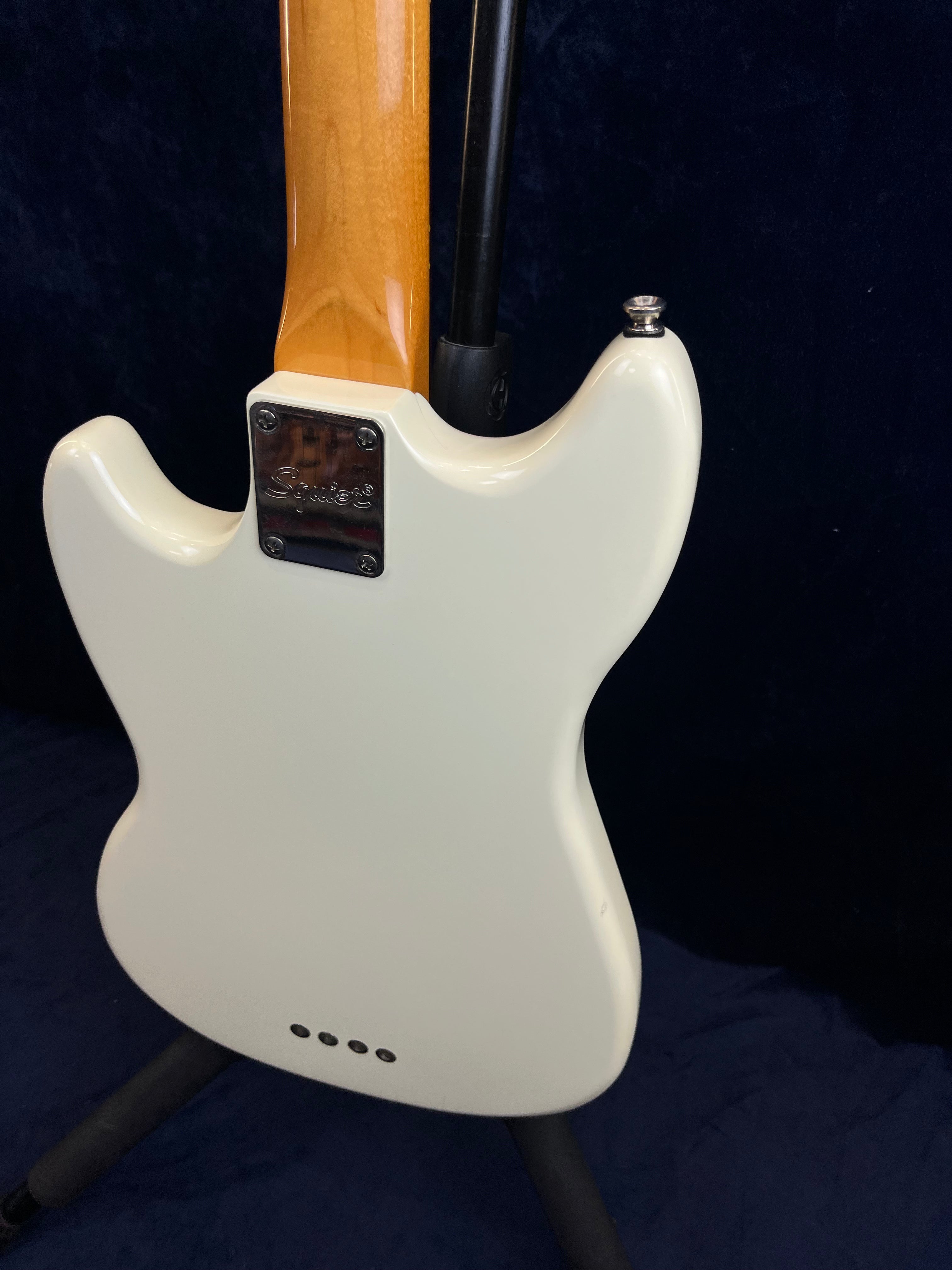 White bass guitar back showing neck joint with a chrome Squier plate, four screw holes at the bottom, and a smooth contoured body shape.