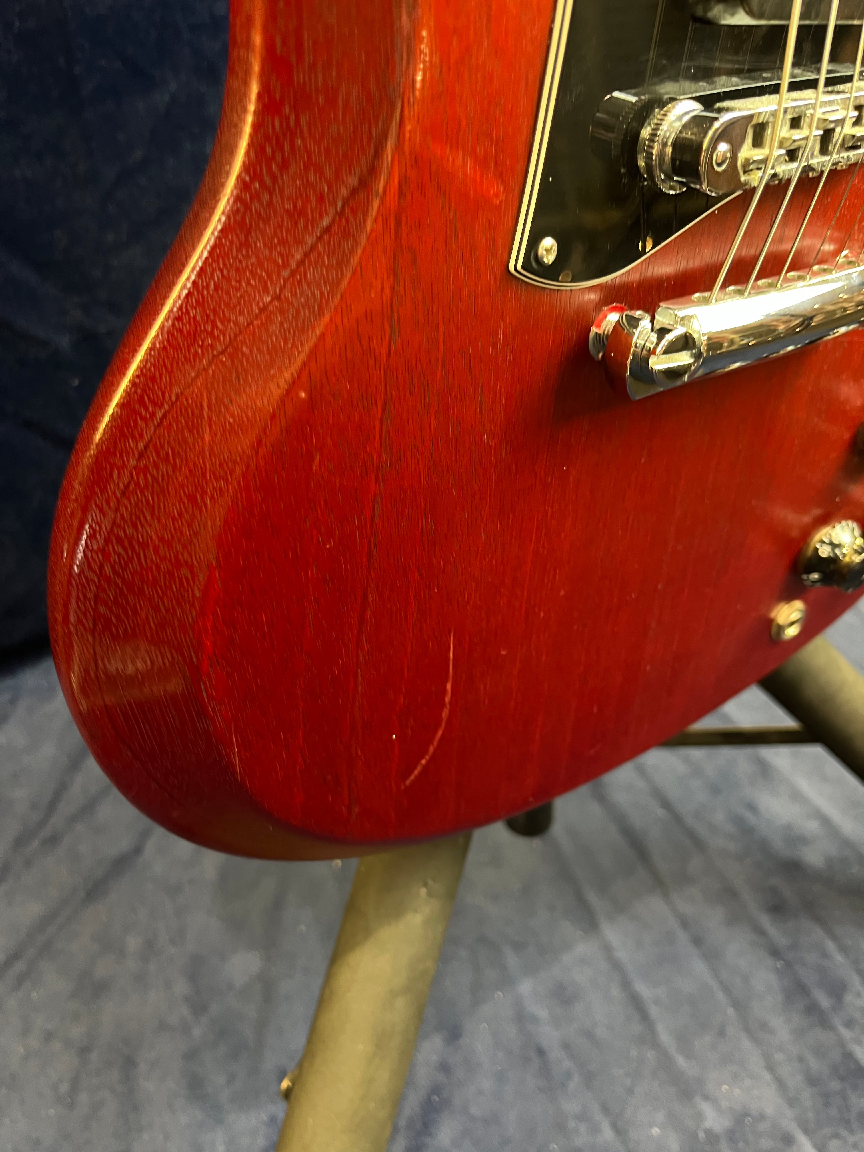 Red electric guitar body close-up, showing a visible scratch near the lower edge and the bridge hardware with strings above it.