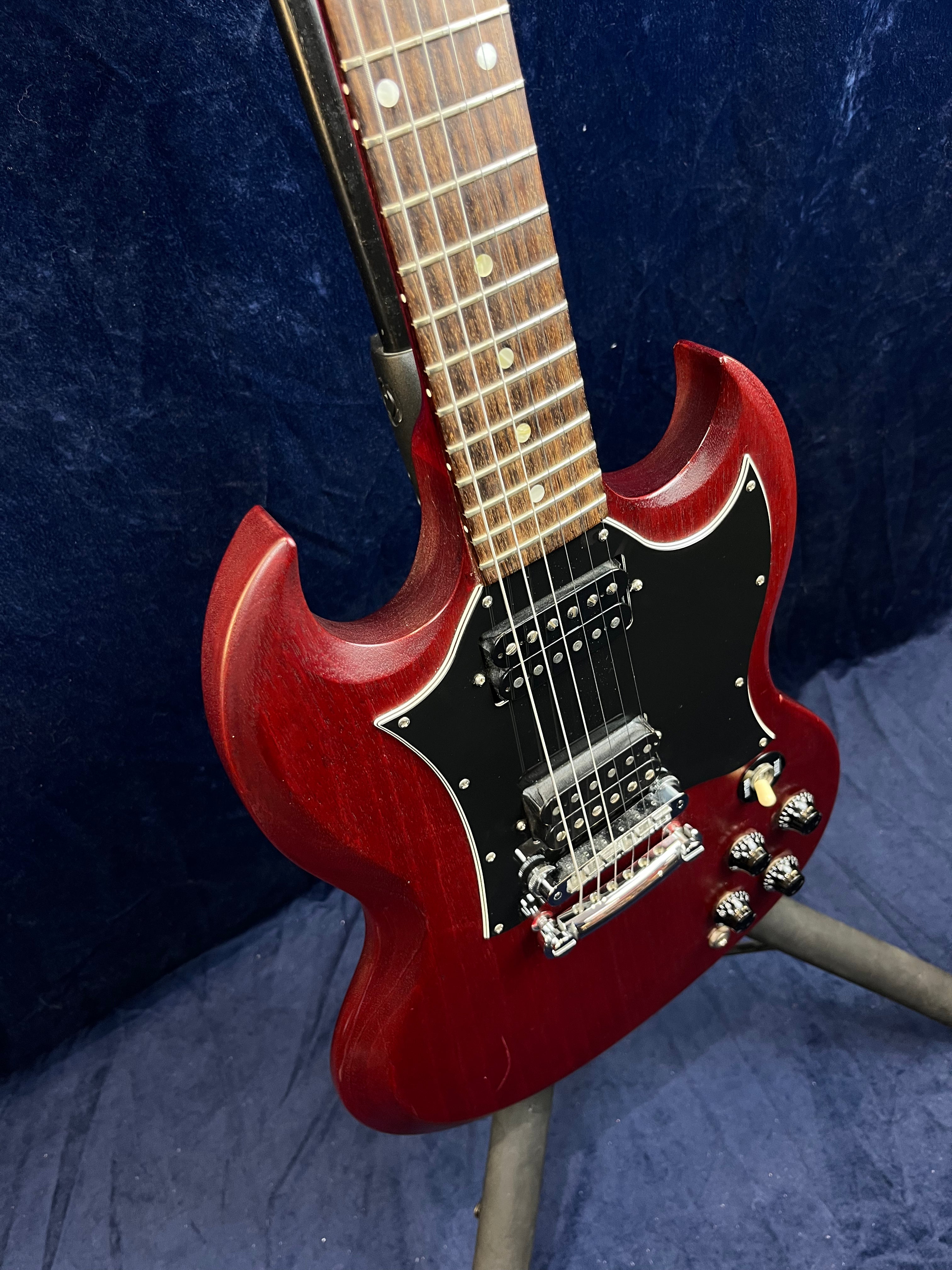 Red electric guitar with a double-cutaway body, black pickguard, two humbucker pickups, four control knobs, and a rosewood fretboard.