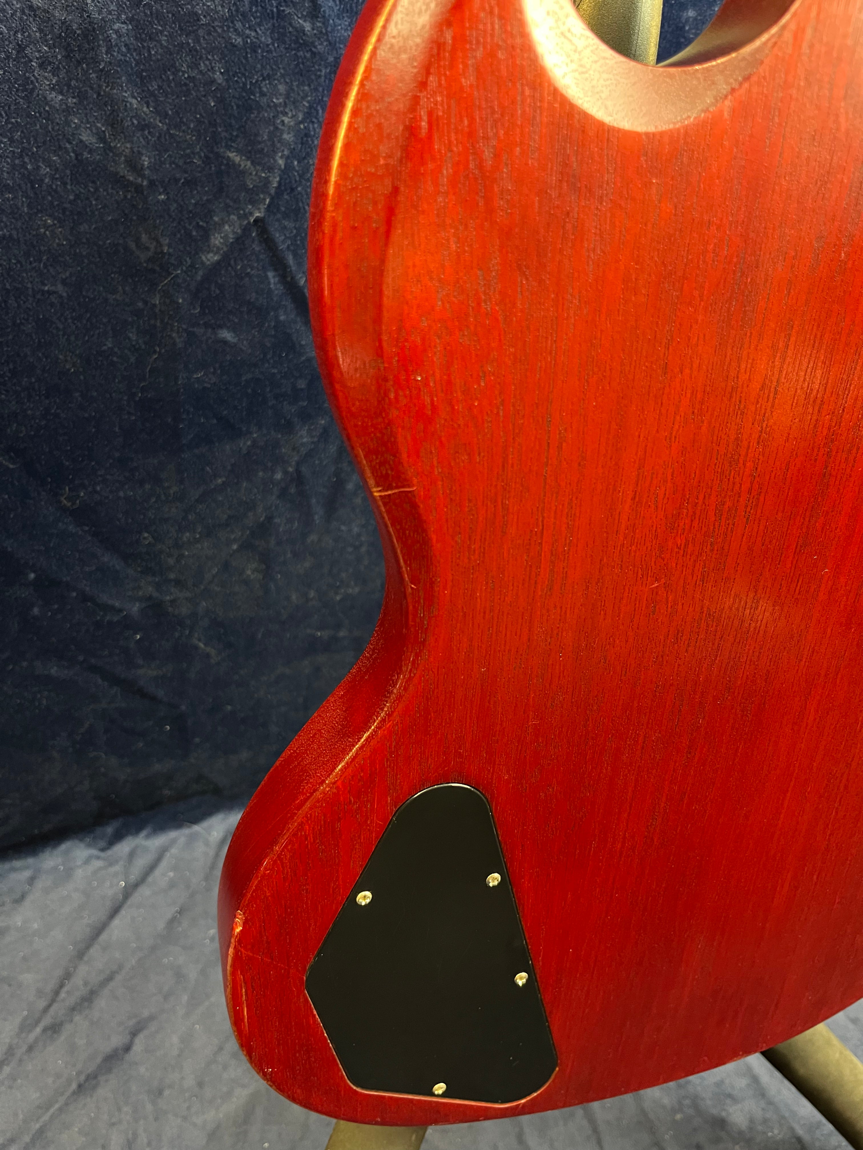 Red electric guitar body with a black plastic cover plate held by screws on the lower back edge.