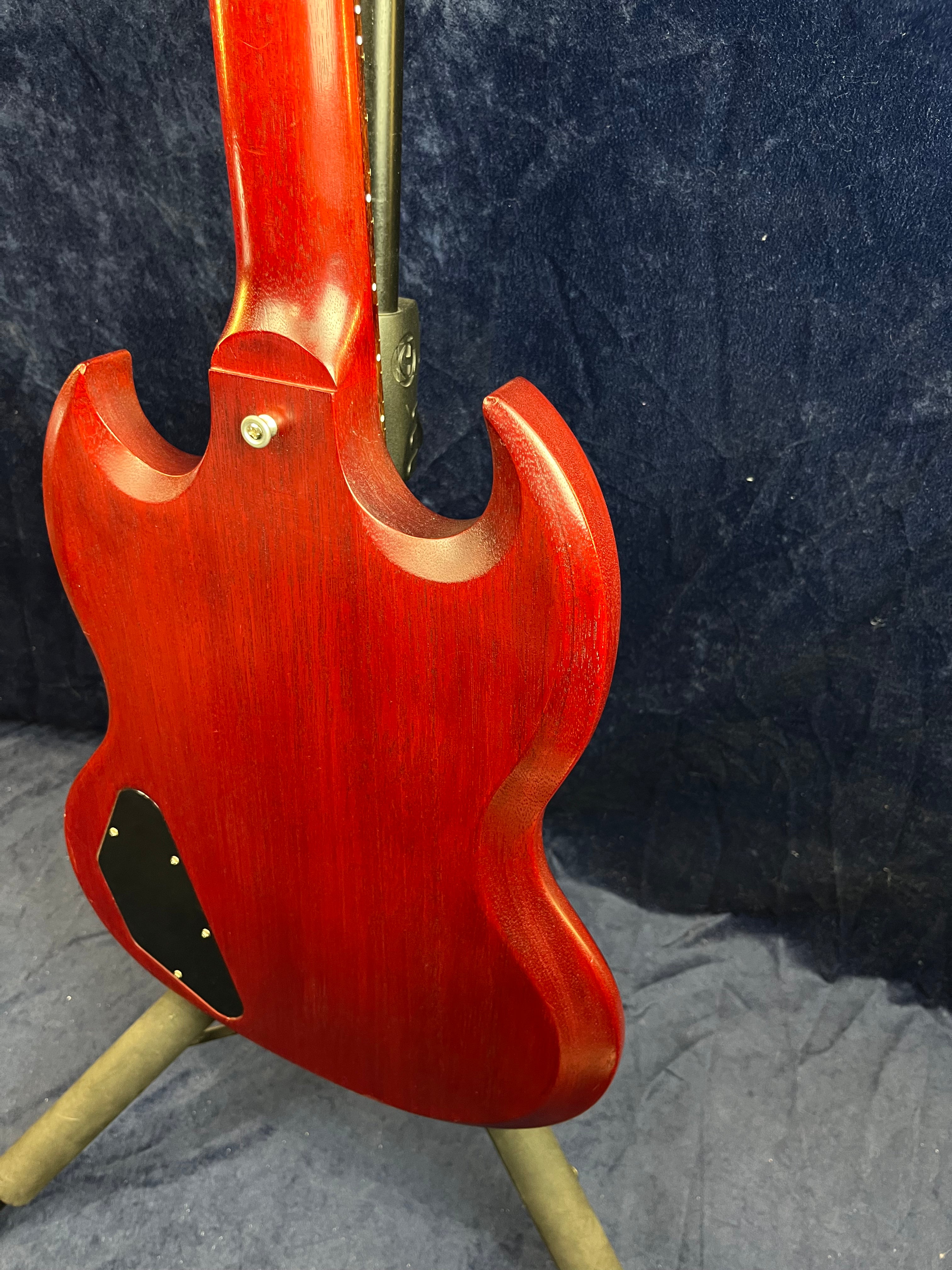 Rear view of a cherry red electric guitar with a double-cutaway body, visible neck joint, and black electronics cover plate on the lower back.