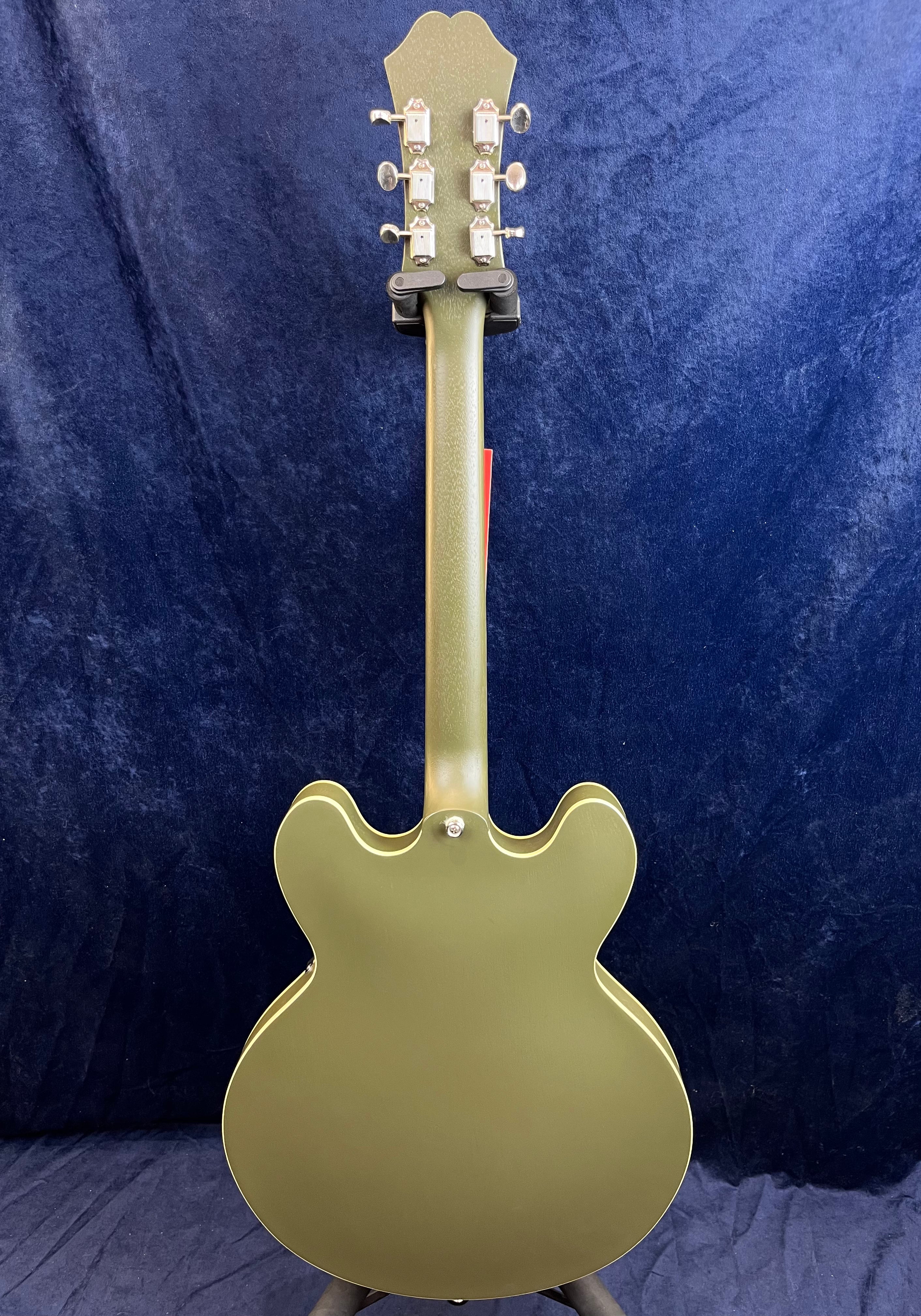 Green double-cutaway electric guitar shown from the back, with six tuning pegs and a metallic finish against a dark blue background.