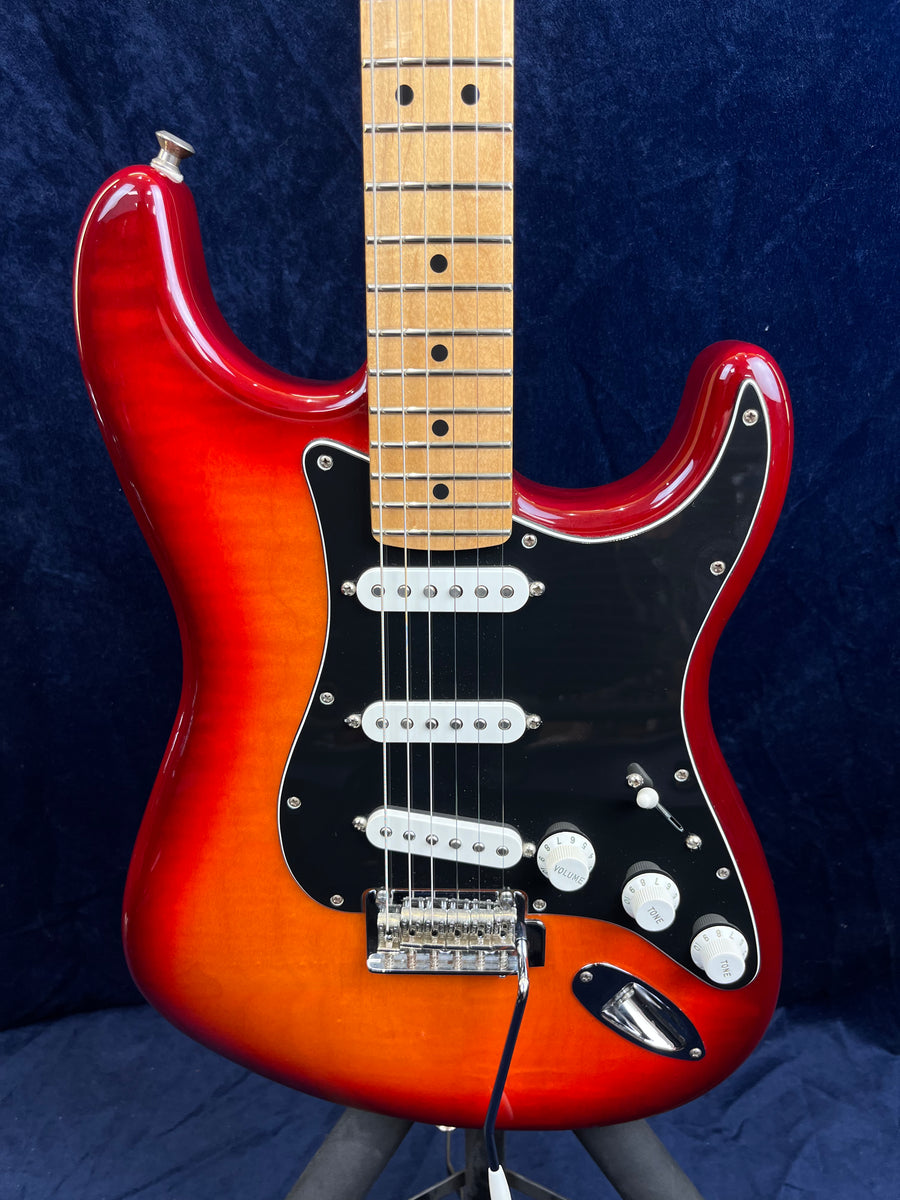 Guitare électrique rouge et orange à trois micros blancs, pickguard noir, touche en érable claire, boutons blancs, câble branché en bas à droite.