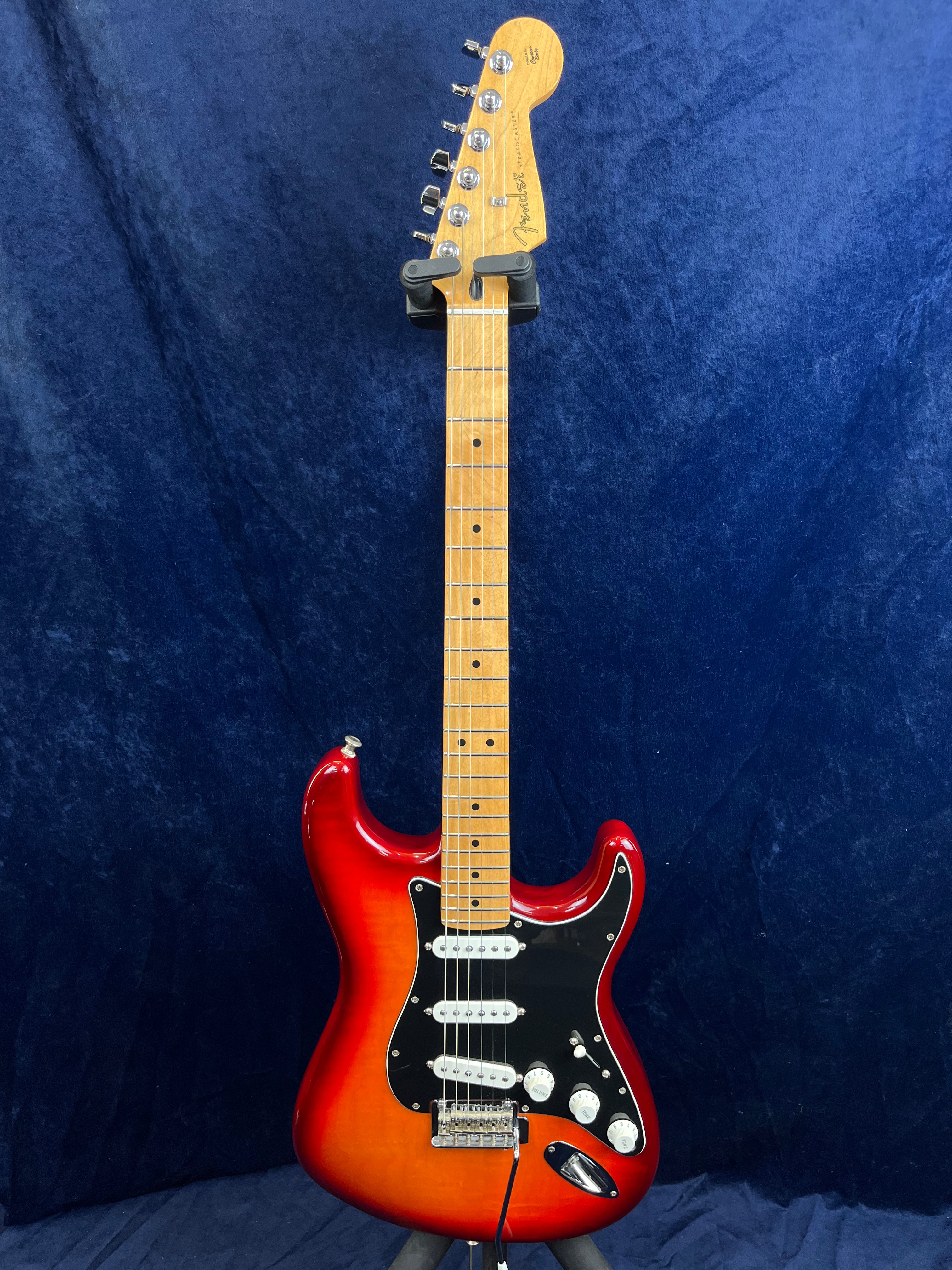 Guitare électrique type Stratocaster, corps rouge dégradé, pickguard noir, trois micros blancs et manche en érable clair.