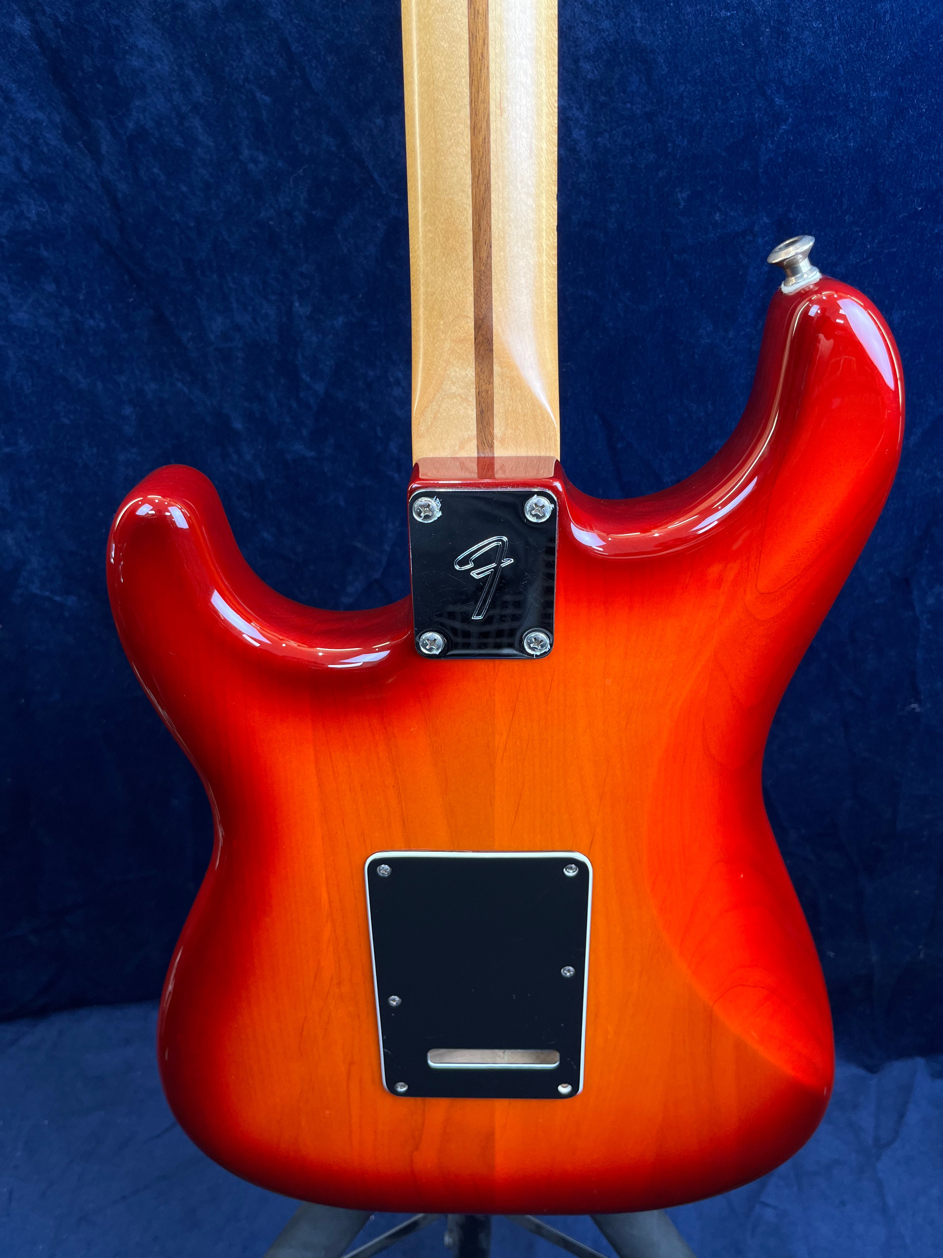 Guitare électrique avec corps rouge sunburst, plaque noire au dos et manche en bois clair traversé par une bande plus foncée.