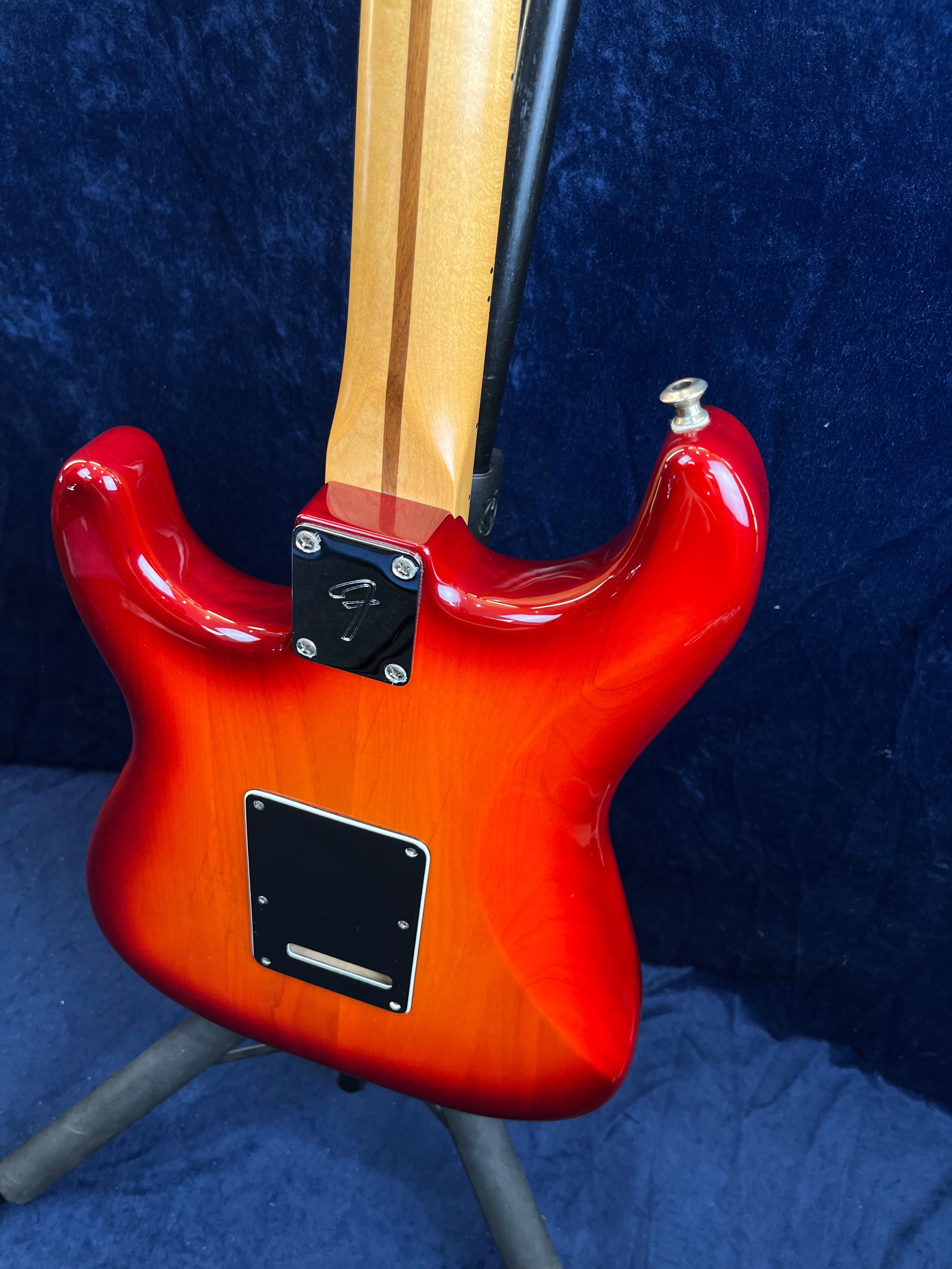 Guitare électrique avec corps rouge dégradé orange et dos verni, manche en bois clair avec une bande sombre, plaques noires fixées par des vis.
