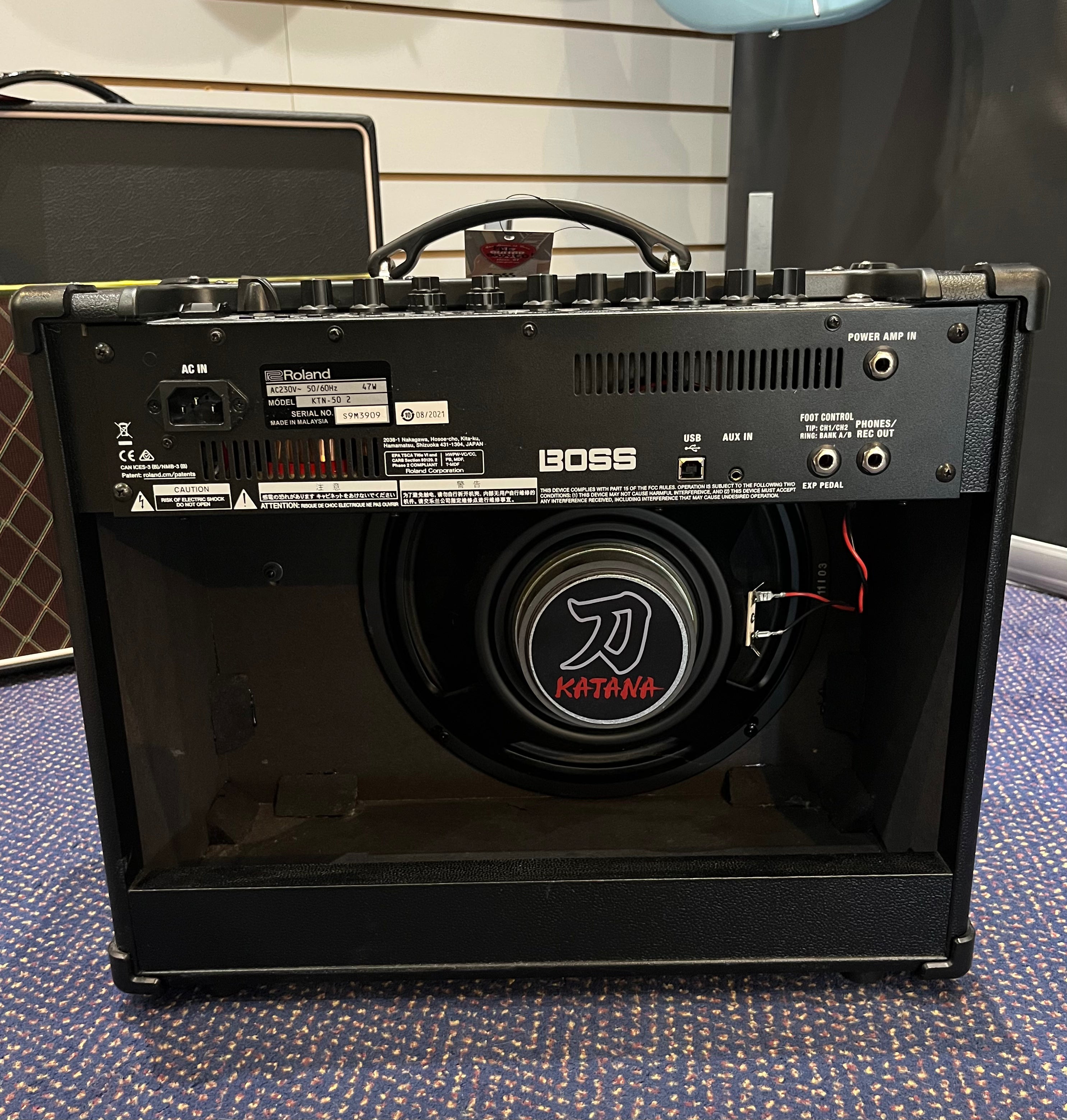 Rear view of a Boss Katana guitar amplifier showing control panel, input/output jacks, and exposed speaker with Katana logo.