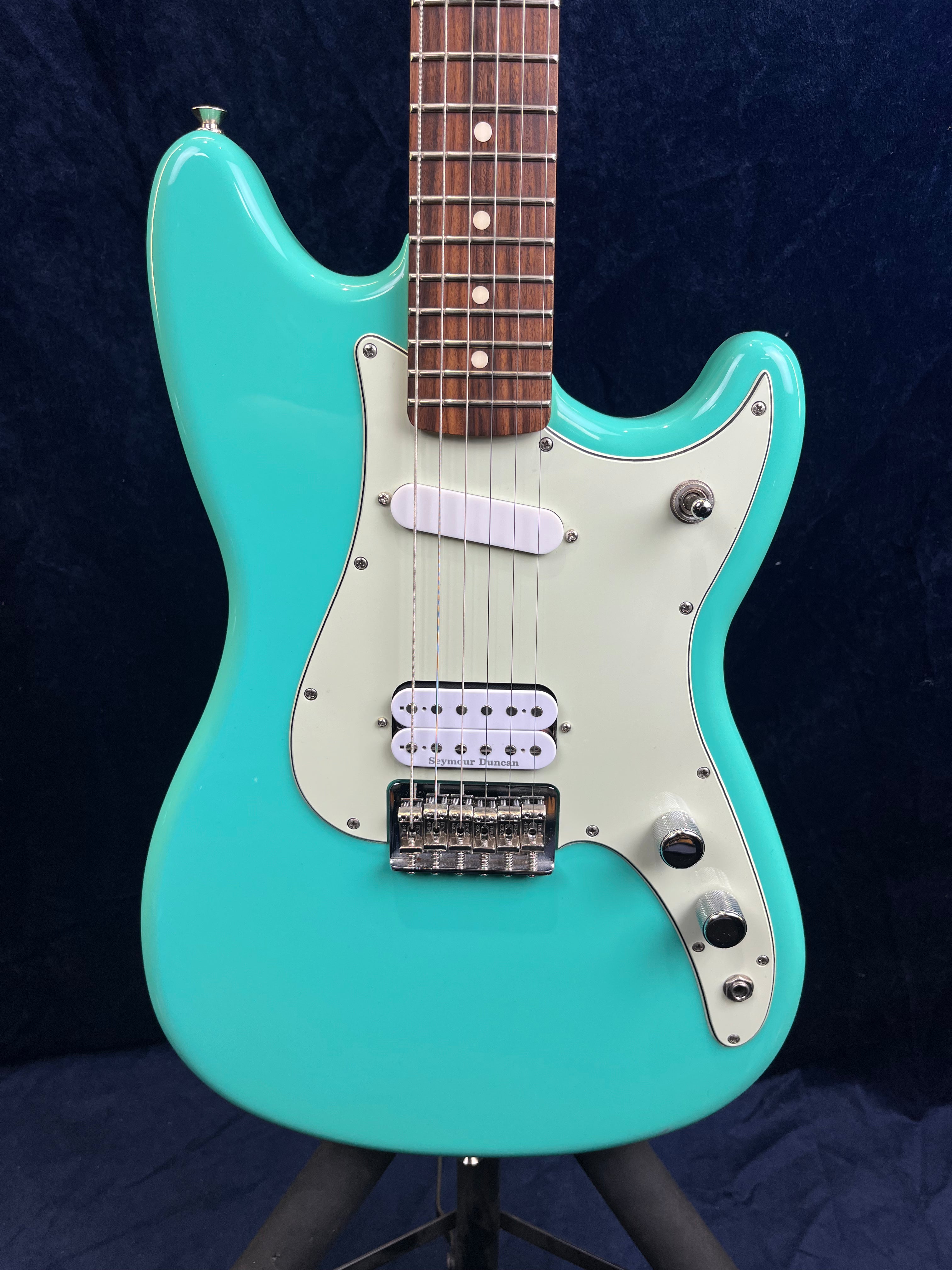 A turquoise electric guitar with a white pickguard, one single-coil and one humbucker pickup, chrome bridge, and two control knobs.