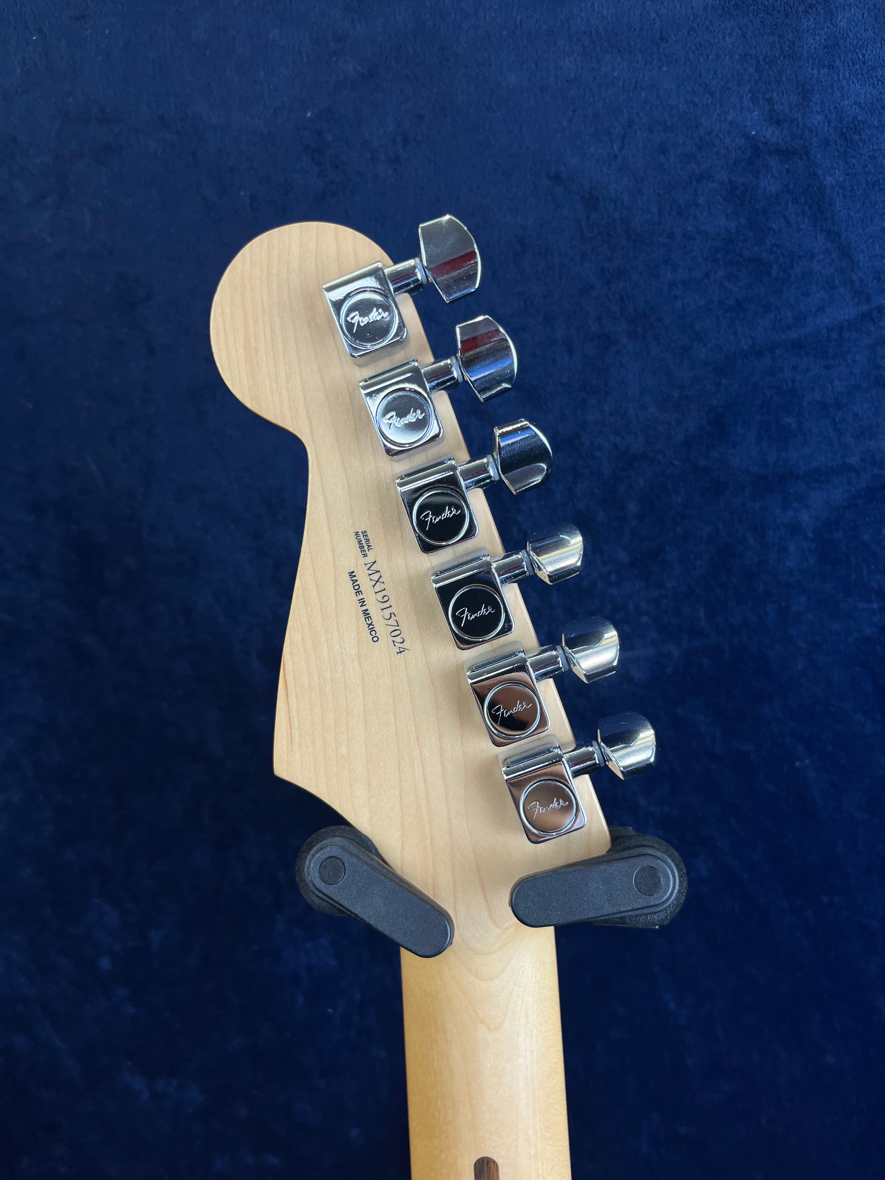 Six chrome Fender tuning pegs on the headstock of a light wood electric guitar, shown against a dark blue background.