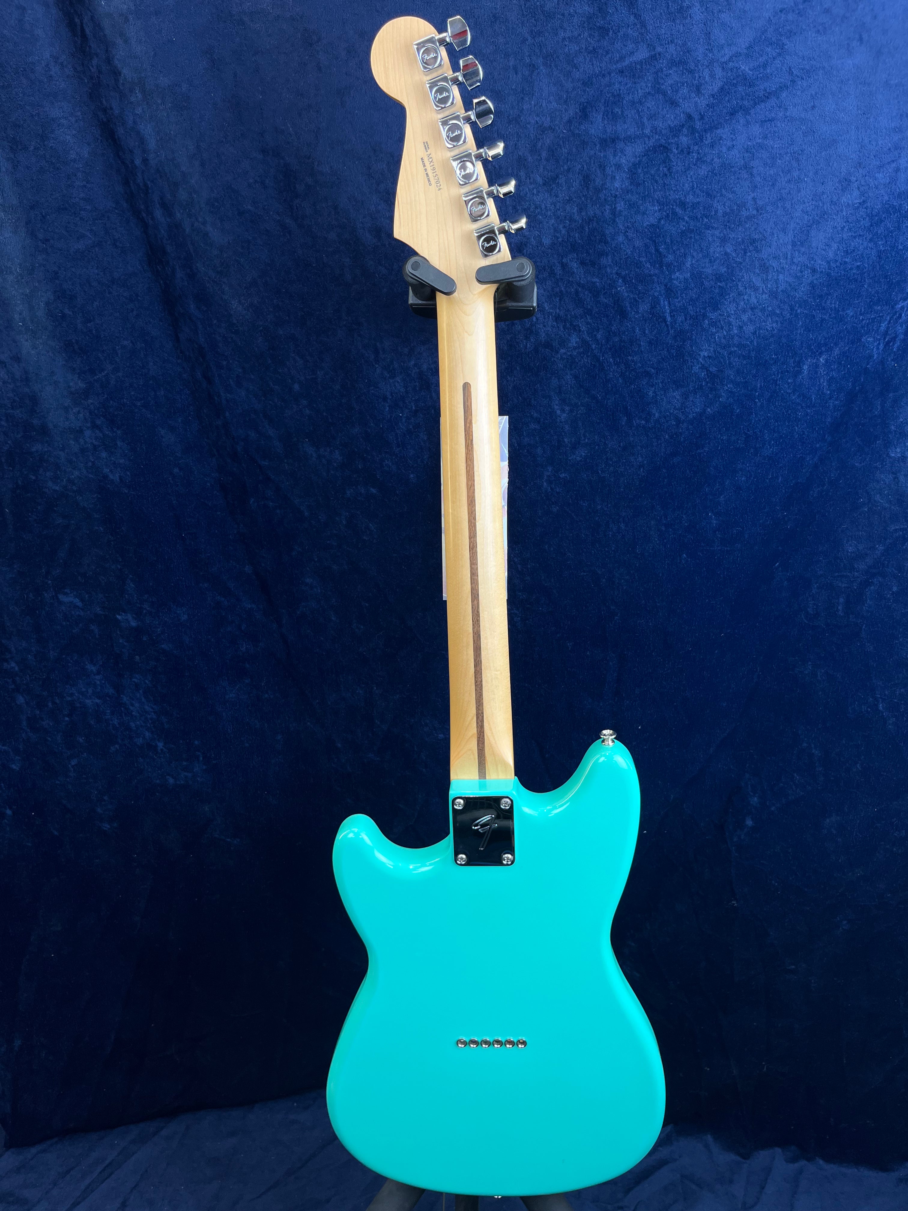 A turquoise electric guitar shown from the back, featuring a light wooden neck and silver tuning pegs against a dark blue background.
