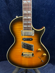 Sunburst Gibson electric guitar with three pickups, two gold control knobs, and a switch on the lower right, featuring a single cutaway body.