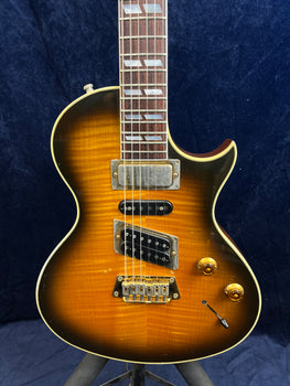 Sunburst Gibson electric guitar with three pickups, two gold control knobs, and a switch on the lower right, featuring a single cutaway body.