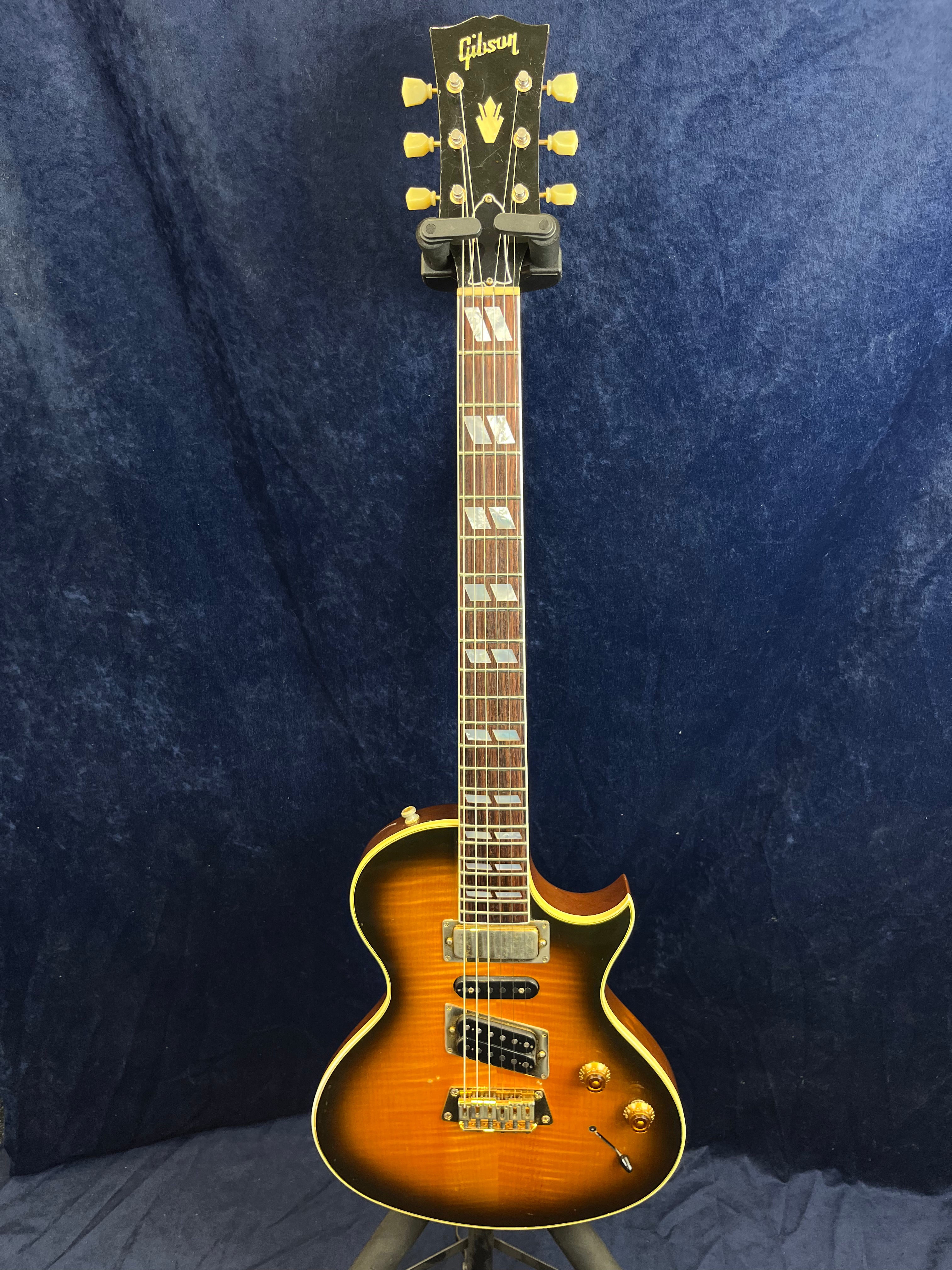 Gibson electric guitar with a sunburst finish, gold hardware, dual humbucker pickups, and two control knobs against a dark blue backdrop.