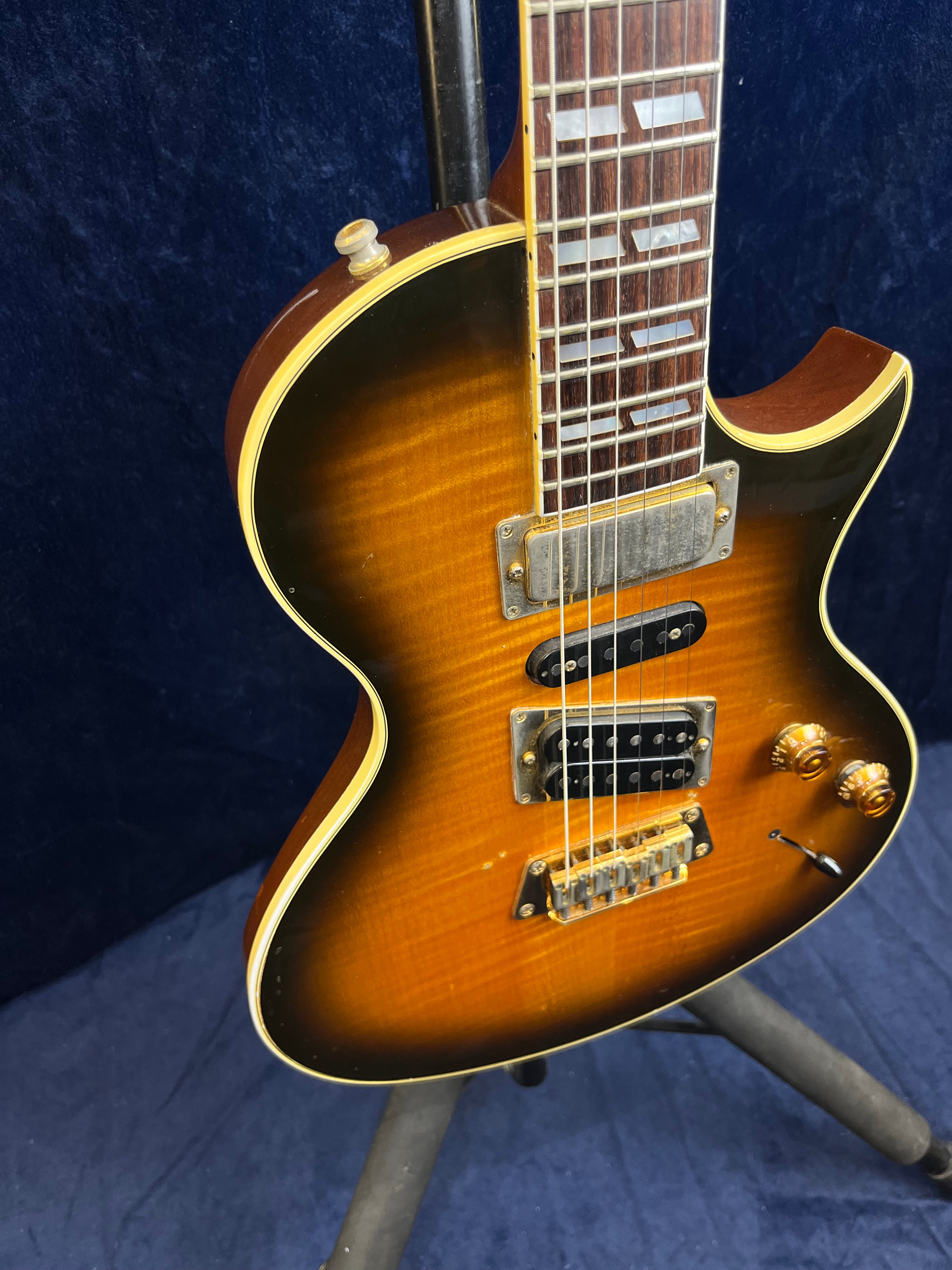 Sunburst Gibson electric guitar with gold hardware, two humbucker pickups, two control knobs, and rectangular mother-of-pearl inlays on the fretboard.