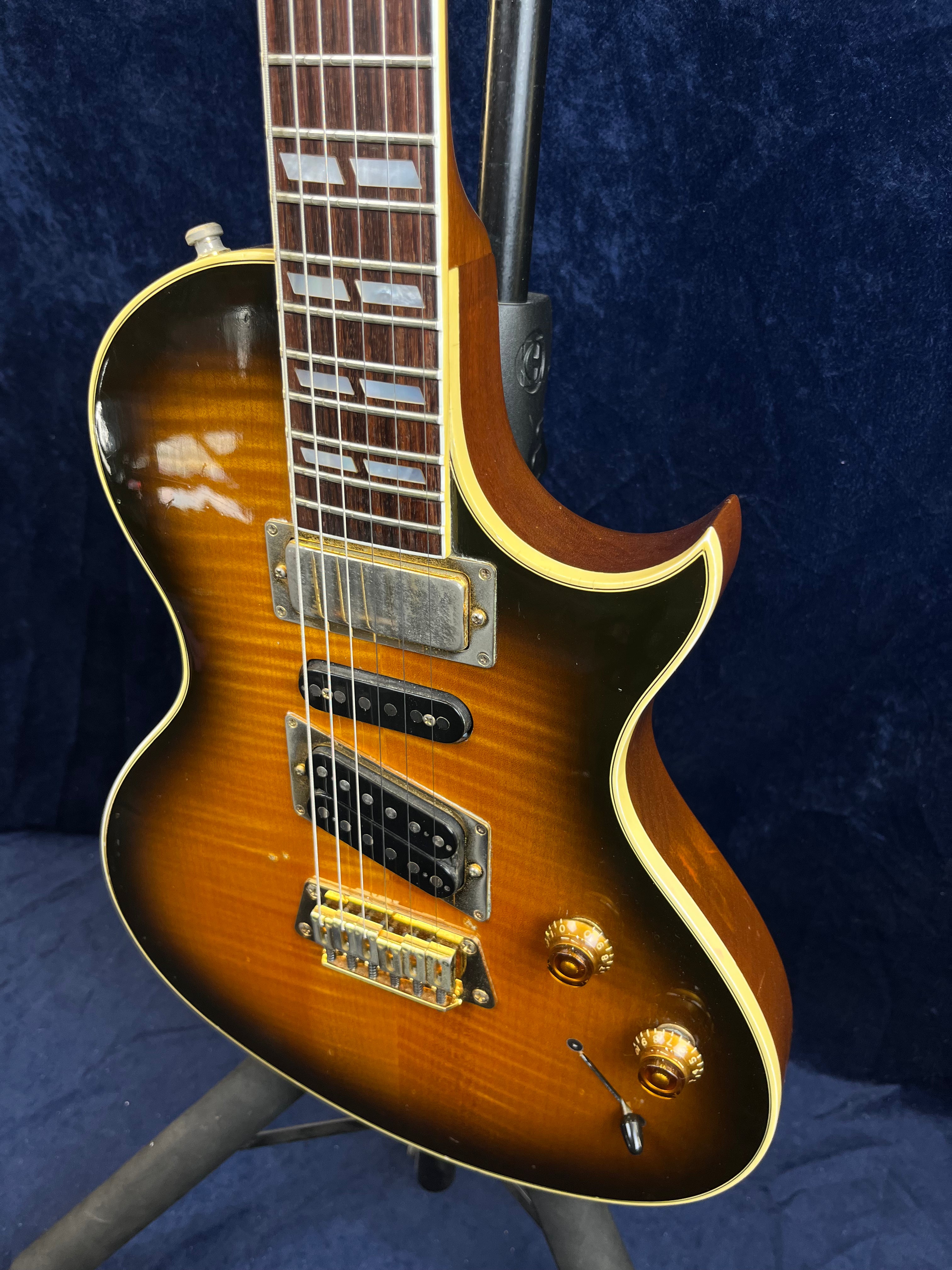 Gibson electric guitar with a sunburst finish, three pickups, gold hardware, two amber control knobs, cream trim, and a dark rosewood fretboard.