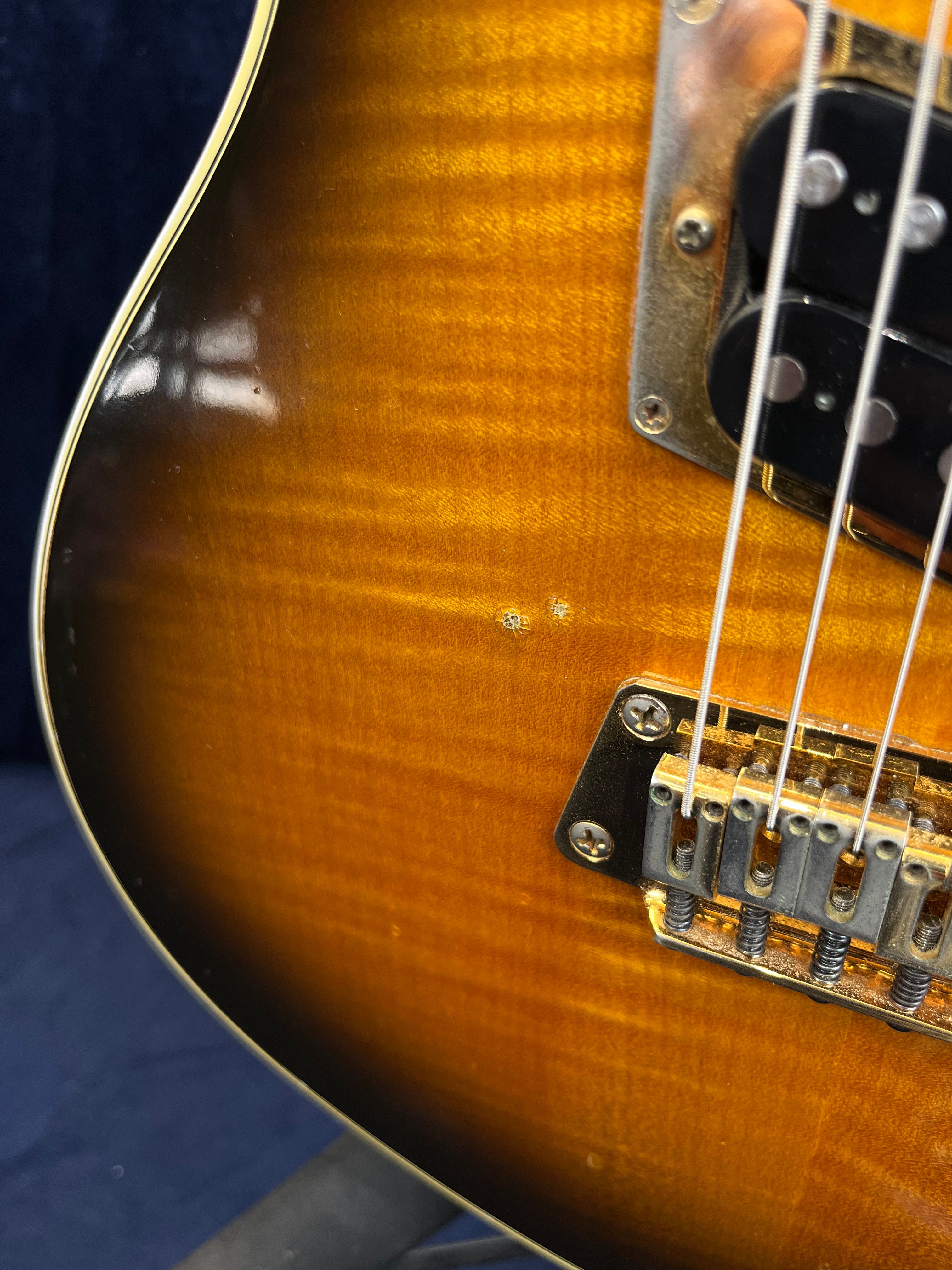 Sunburst Gibson electric guitar body close-up showing strings, bridge, pickup, and two small dents in the wood finish.