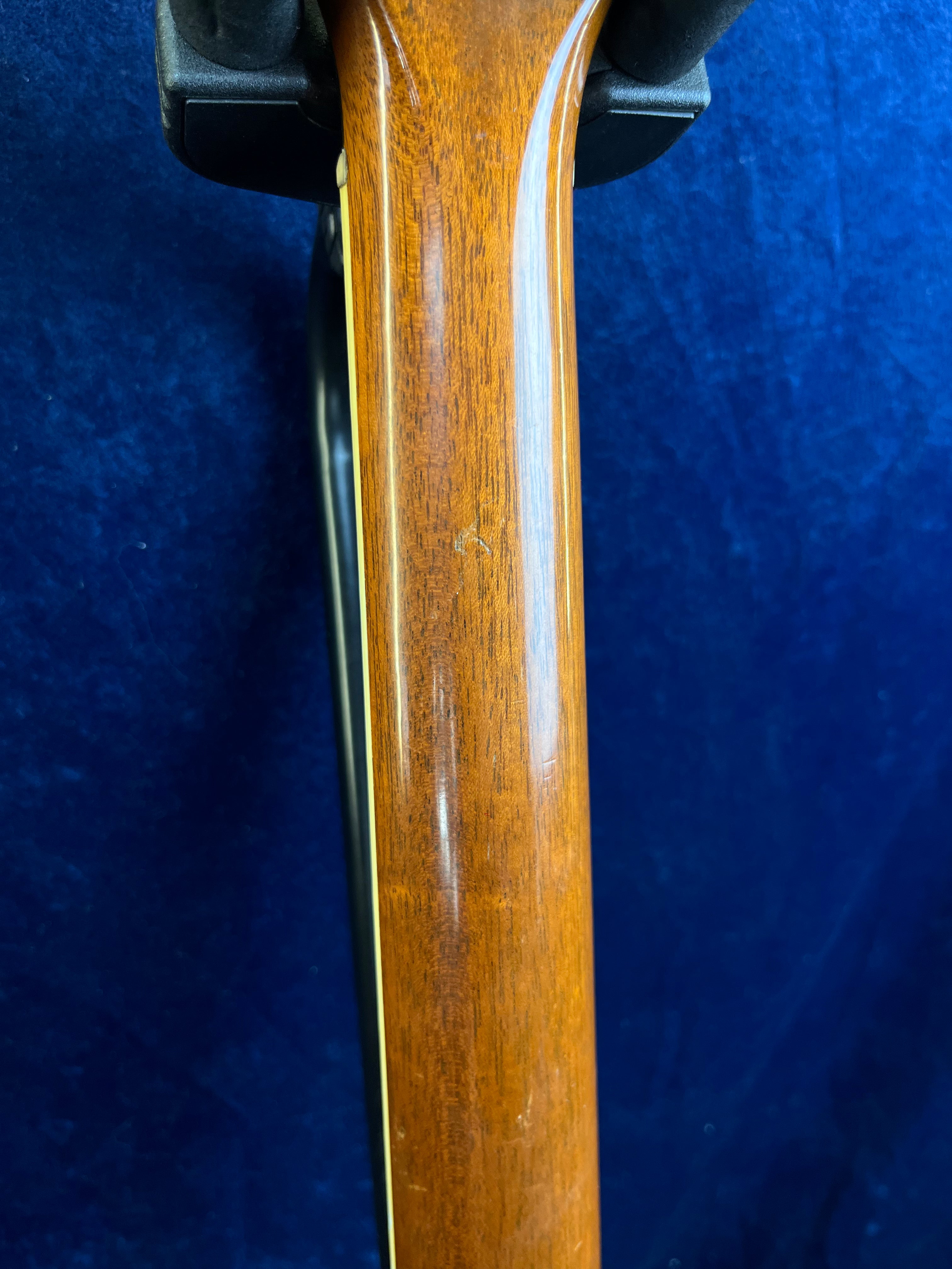 Smooth, polished wooden neck of a Gibson guitar against a rich blue background, showing subtle grain and minor surface marks.
