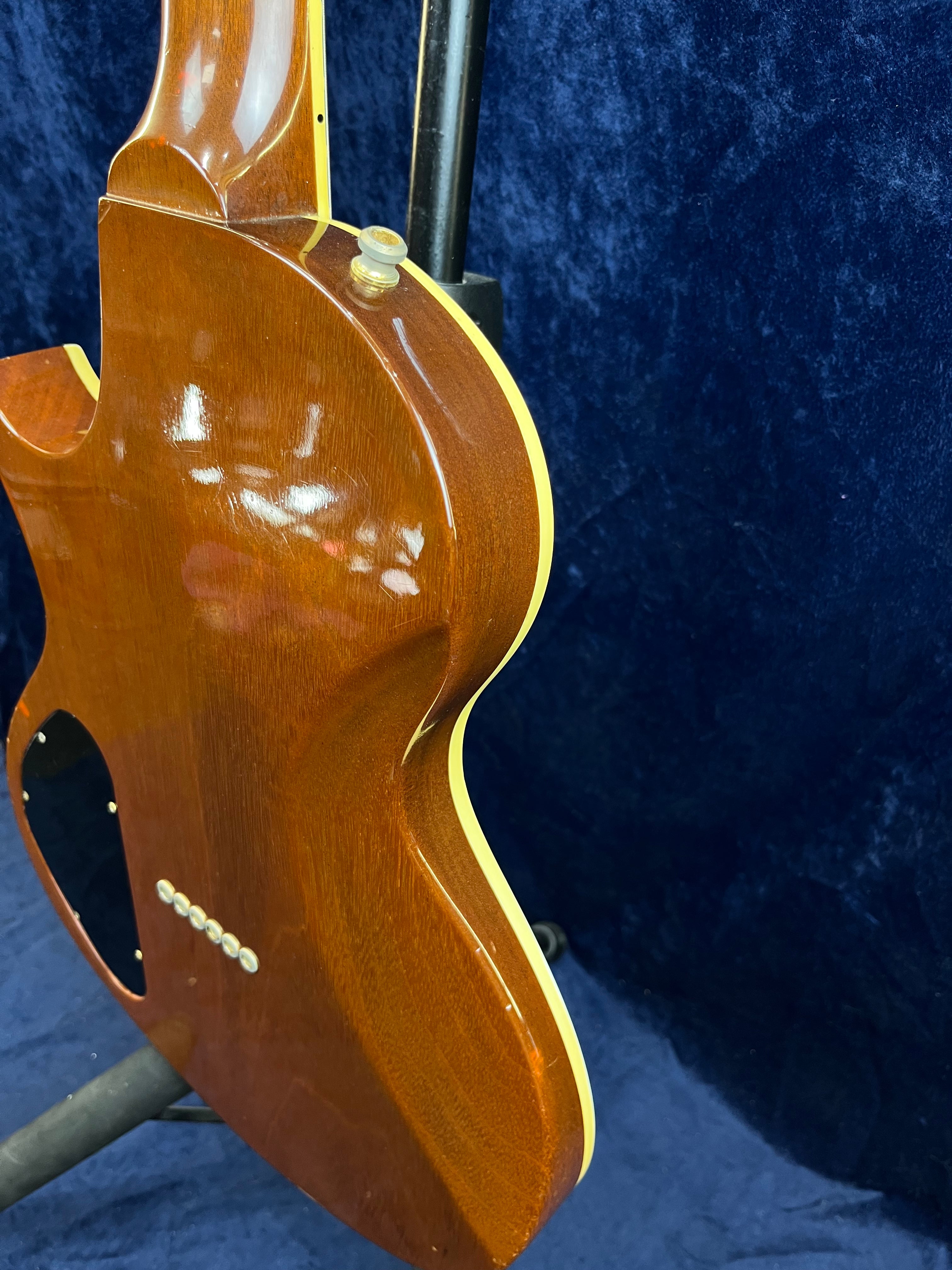 Back side of a Gibson electric guitar showing glossy brown wood, cream binding, a strap button, and control plate against a dark blue background.