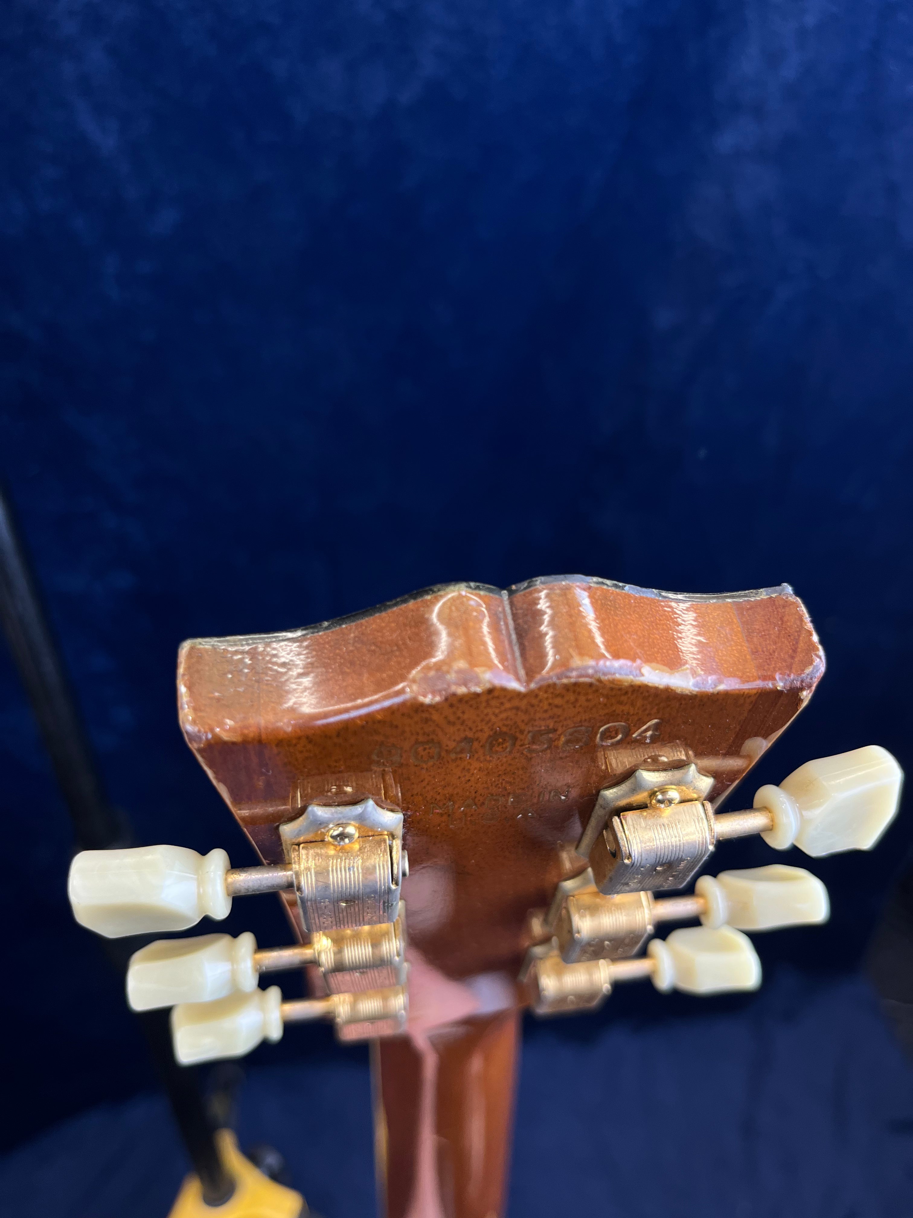 Closeup of the back of a Gibson guitar headstock showing worn wood, visible serial number, and vintage-style tuning pegs with white knobs.
