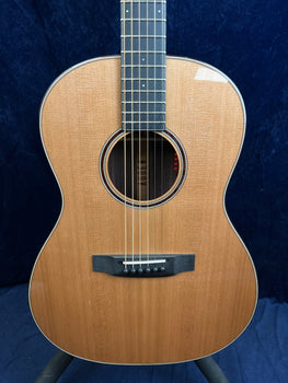 Guitare acoustique à six cordes, caisse en bois clair, rosace ronde décorée, chevalet noir et touche foncée, fond bleu uni en arrière-plan.