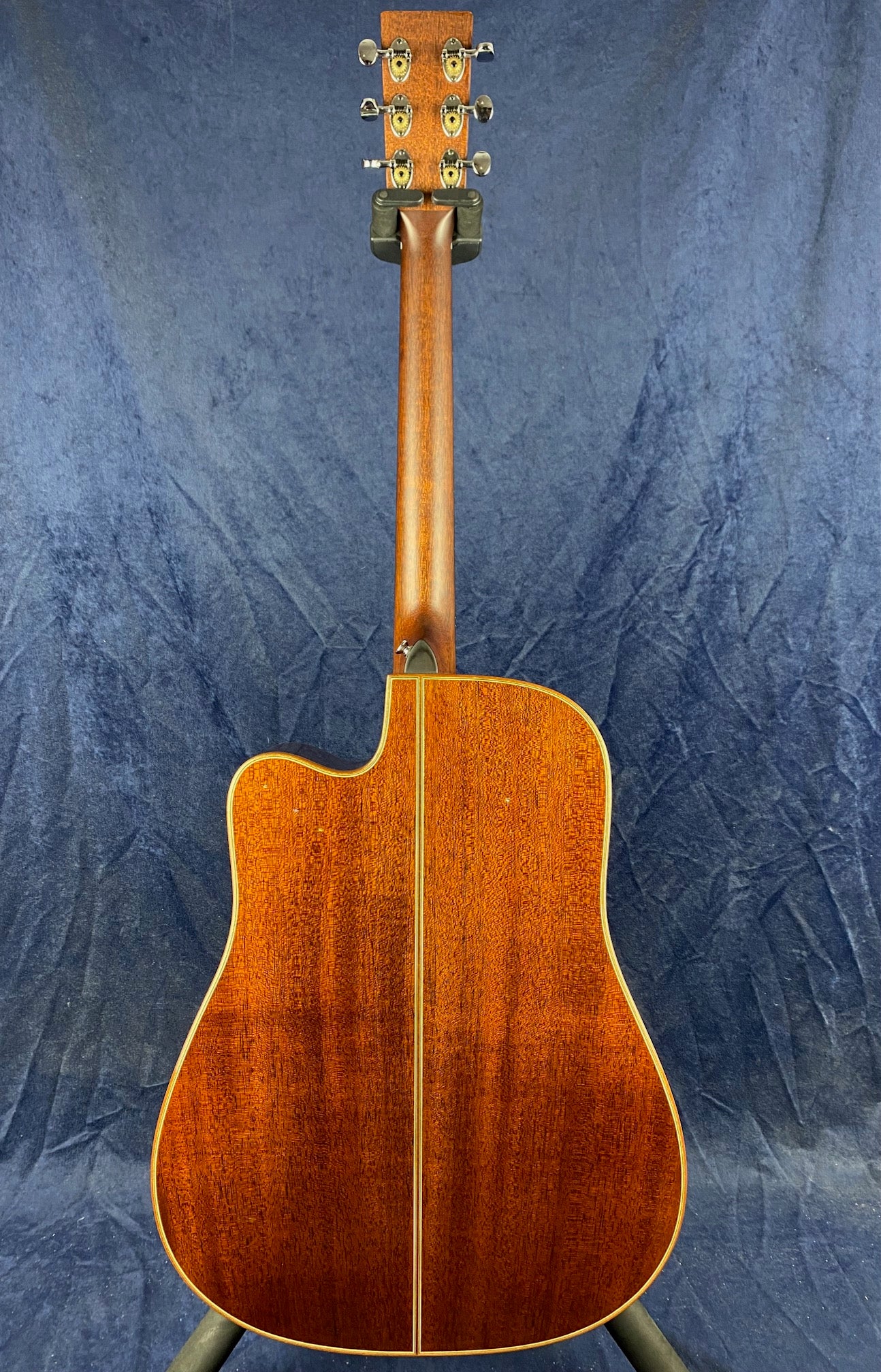 Mahogany acoustic guitar shown from the back, with a natural wood finish, single cutaway body, and gold tuning pegs visible on the headstock.