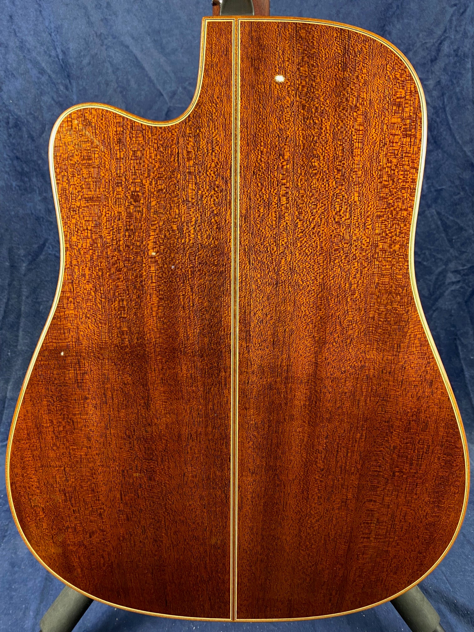 Back of an acoustic guitar showing rich, reddish-brown wood grain, a thin center strip, and cream binding along the edges.