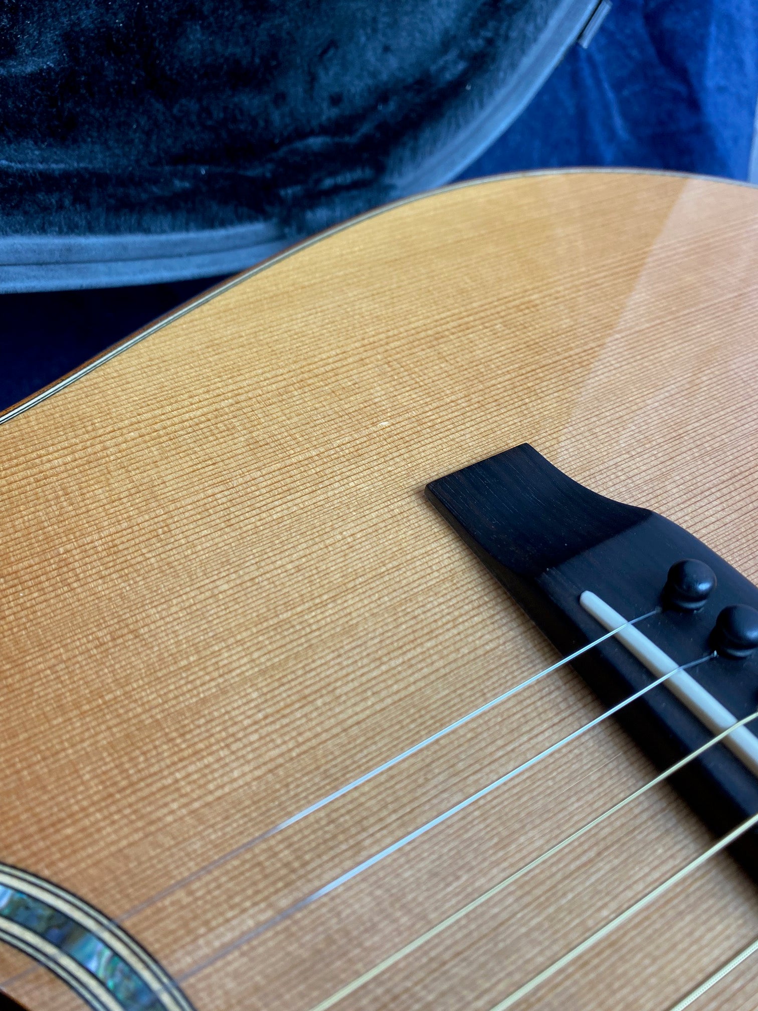Close-up of an acoustic guitar’s wooden body, bridge, and strings, with part of a plush-lined guitar case in the background.