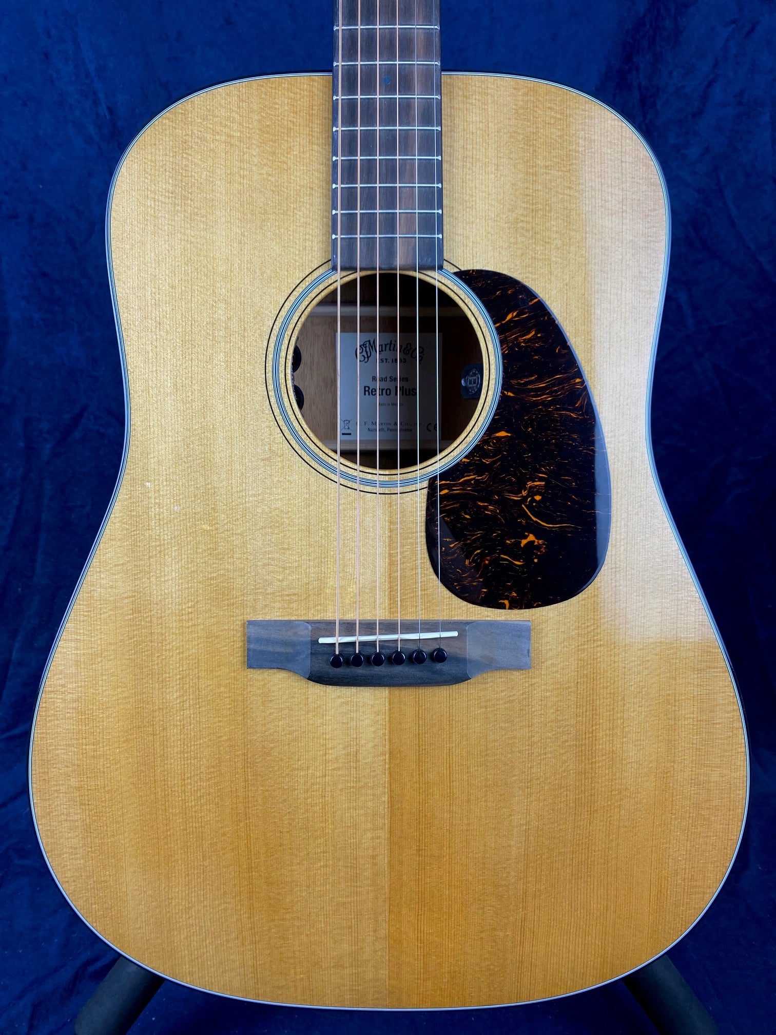 Light wood acoustic guitar with six strings, a tortoiseshell-patterned pickguard, circular sound hole, black bridge pins, and visible wood grain.