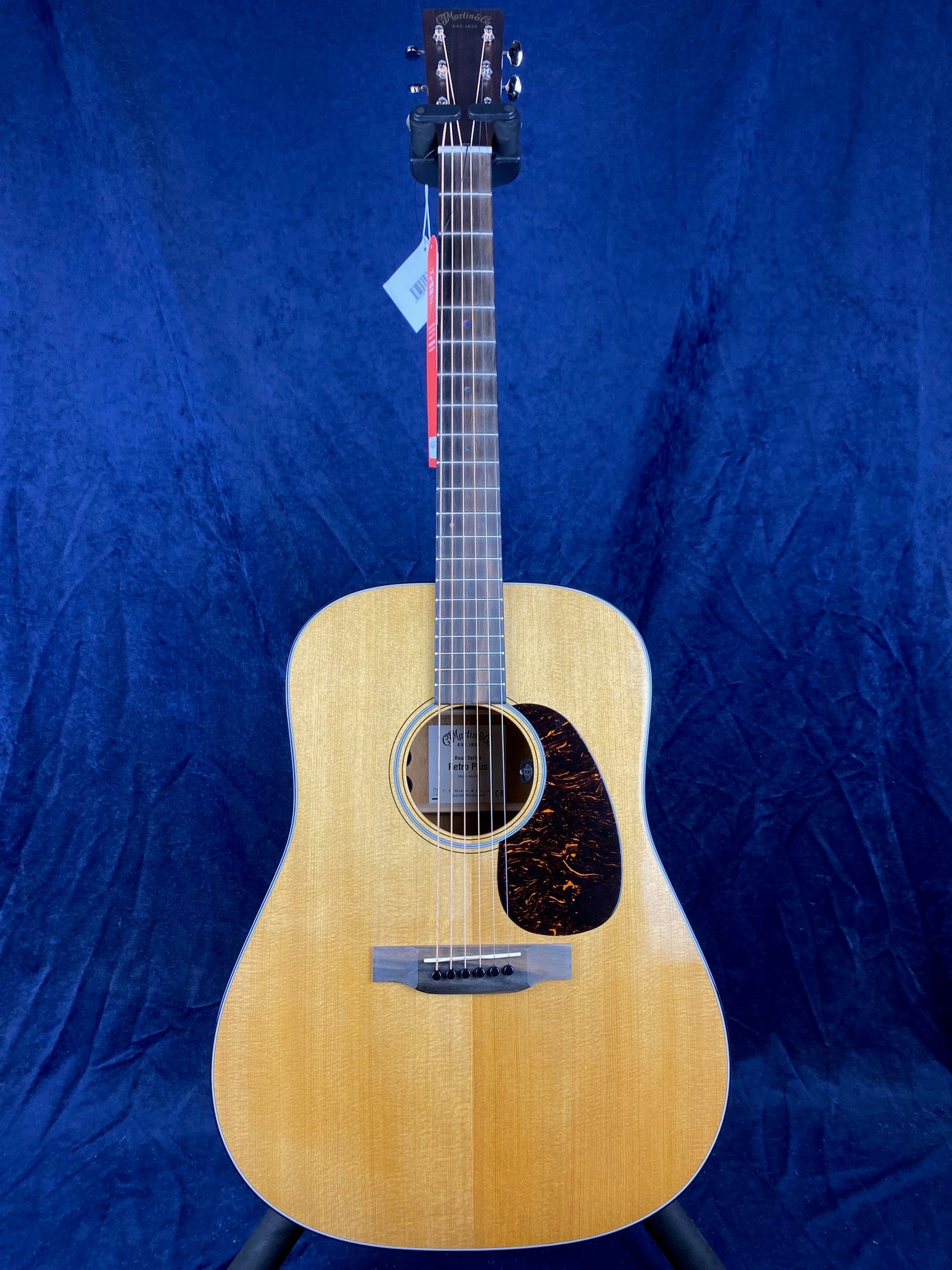 Natural wood acoustic guitar with a dark tortoiseshell pickguard, six strings, and a Martin & Co. logo on the headstock against a blue background.