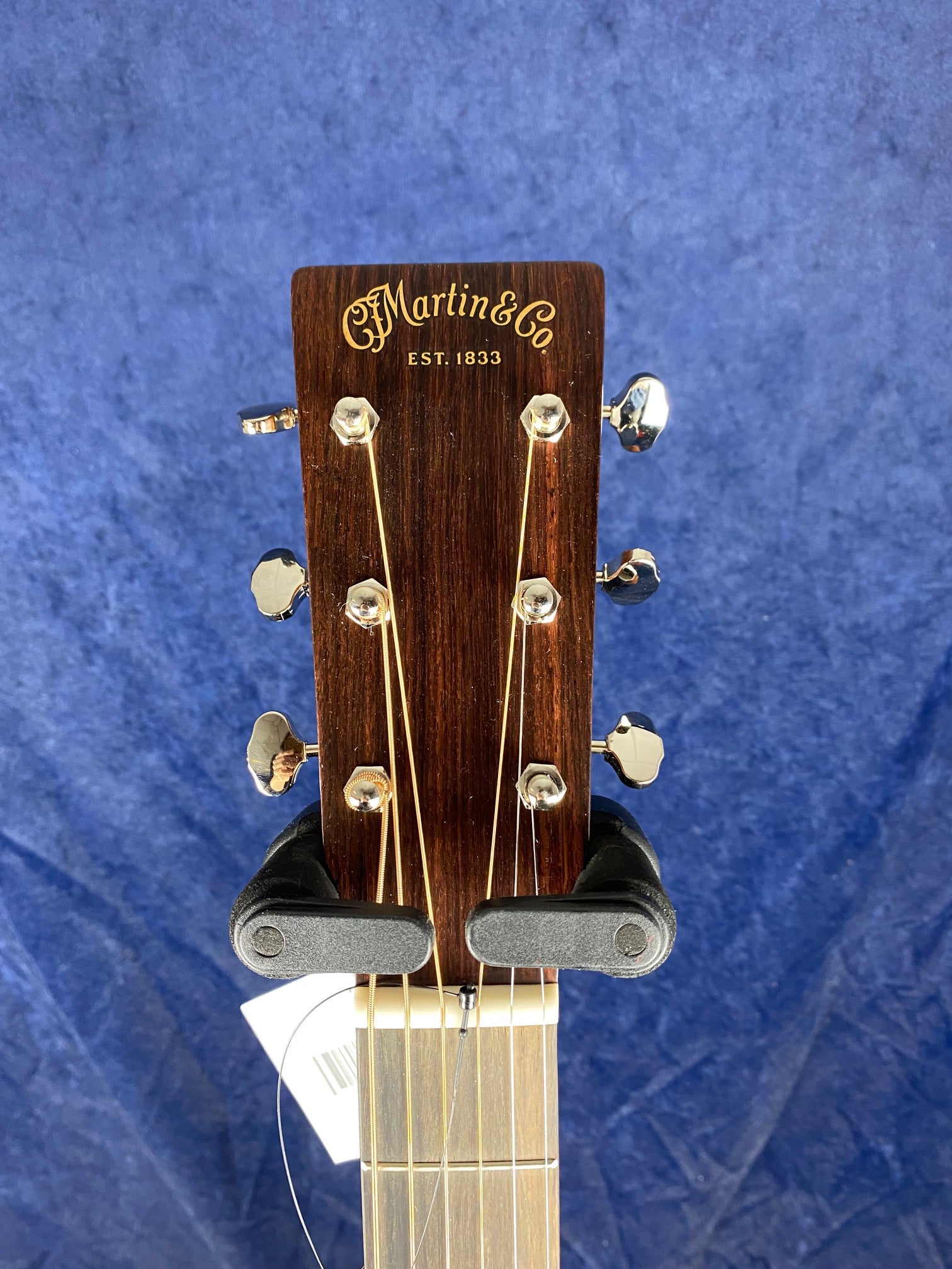 Headstock of a Martin & Co acoustic guitar with six tuning pegs, gold logo, and strings, set against a blue textured background.