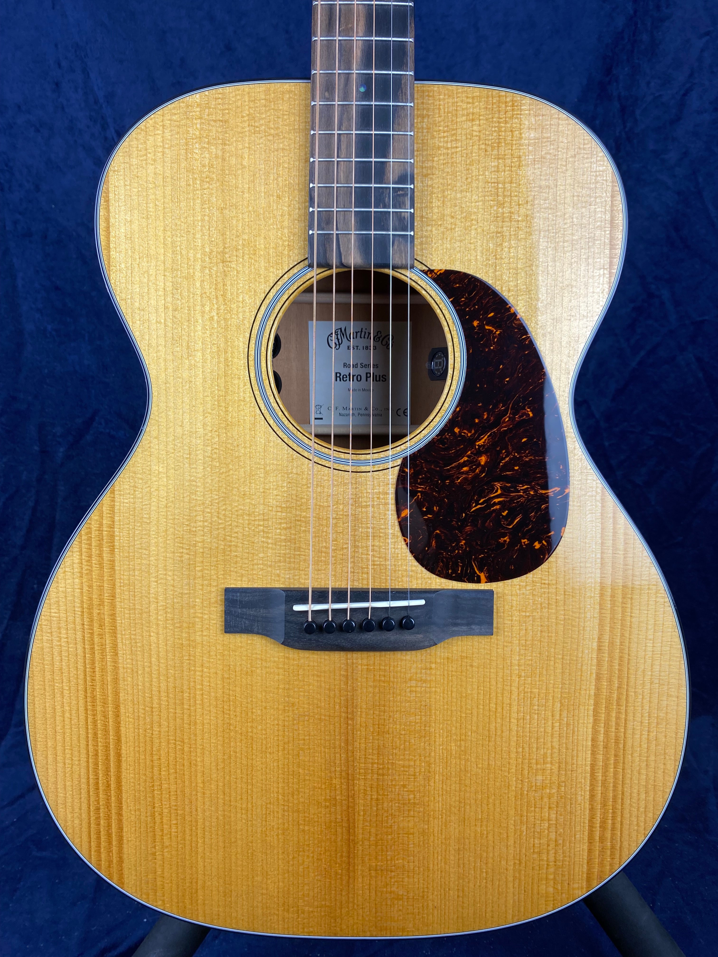 Light wood acoustic guitar with six strings, a dark wood bridge, and a tortoiseshell-patterned pickguard on the right side of the sound hole.