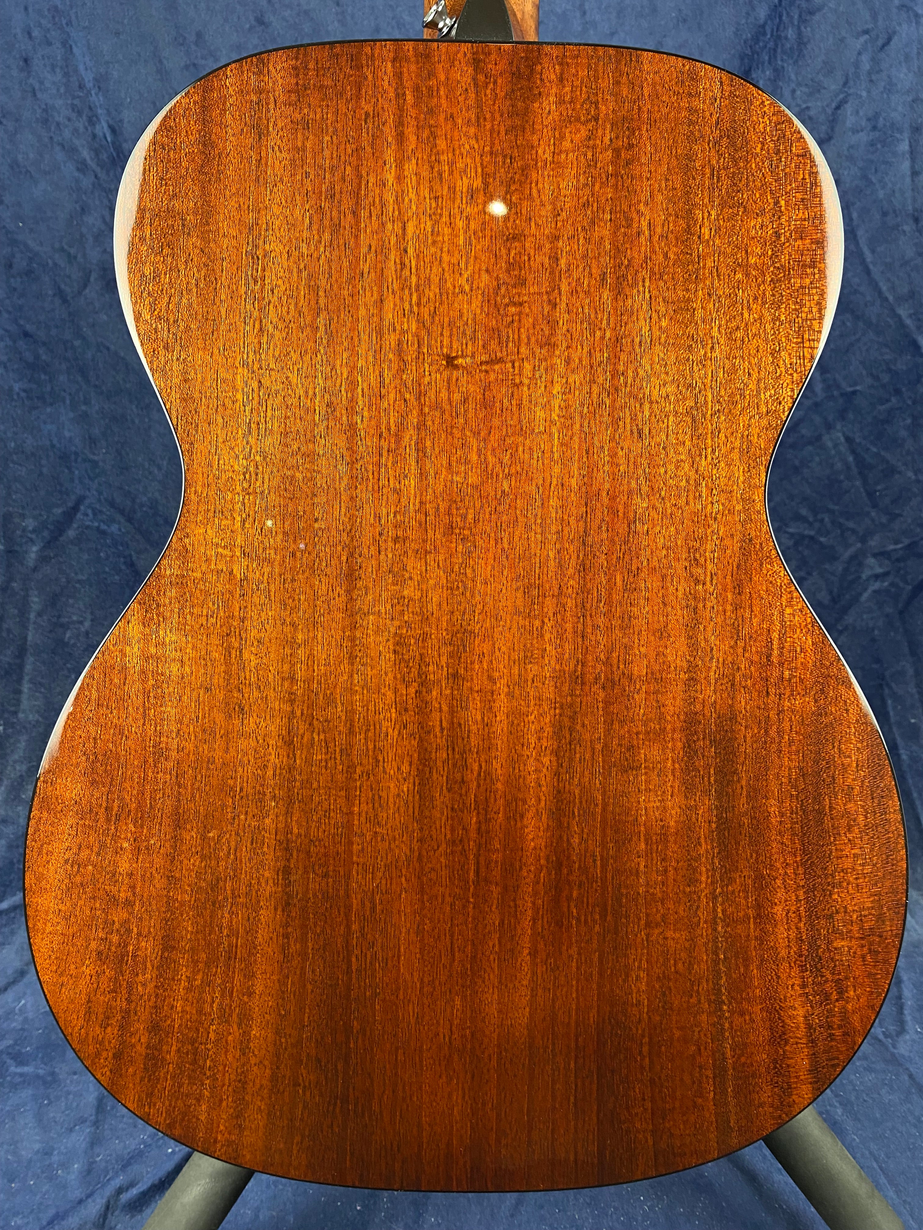 The back of an acoustic guitar made of rich brown wood, featuring a smooth grain and a small white mark near the top center.