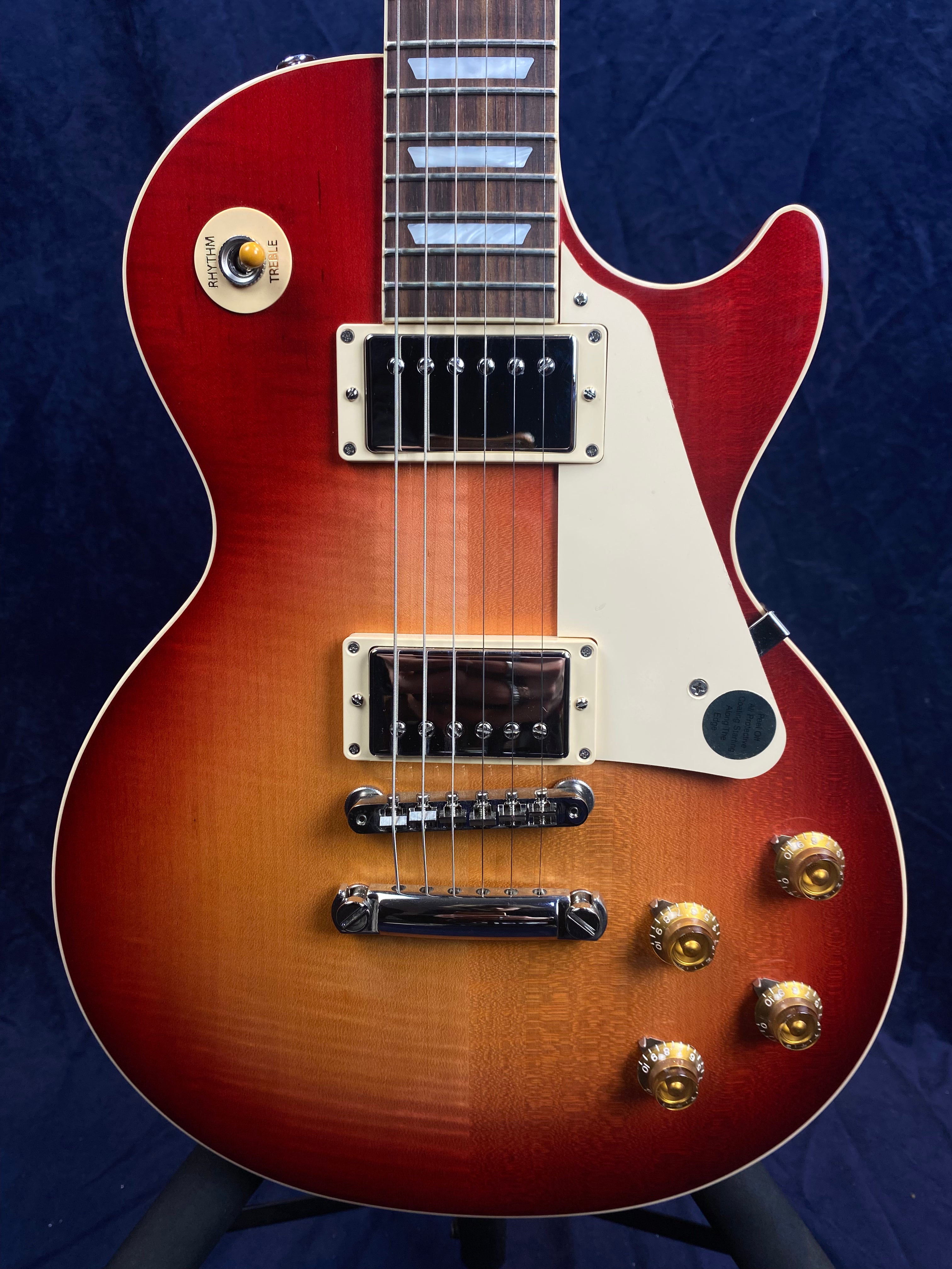 Electric guitar with a sunburst red to amber finish, two chrome pickups, four gold control knobs, and a cream pickguard.