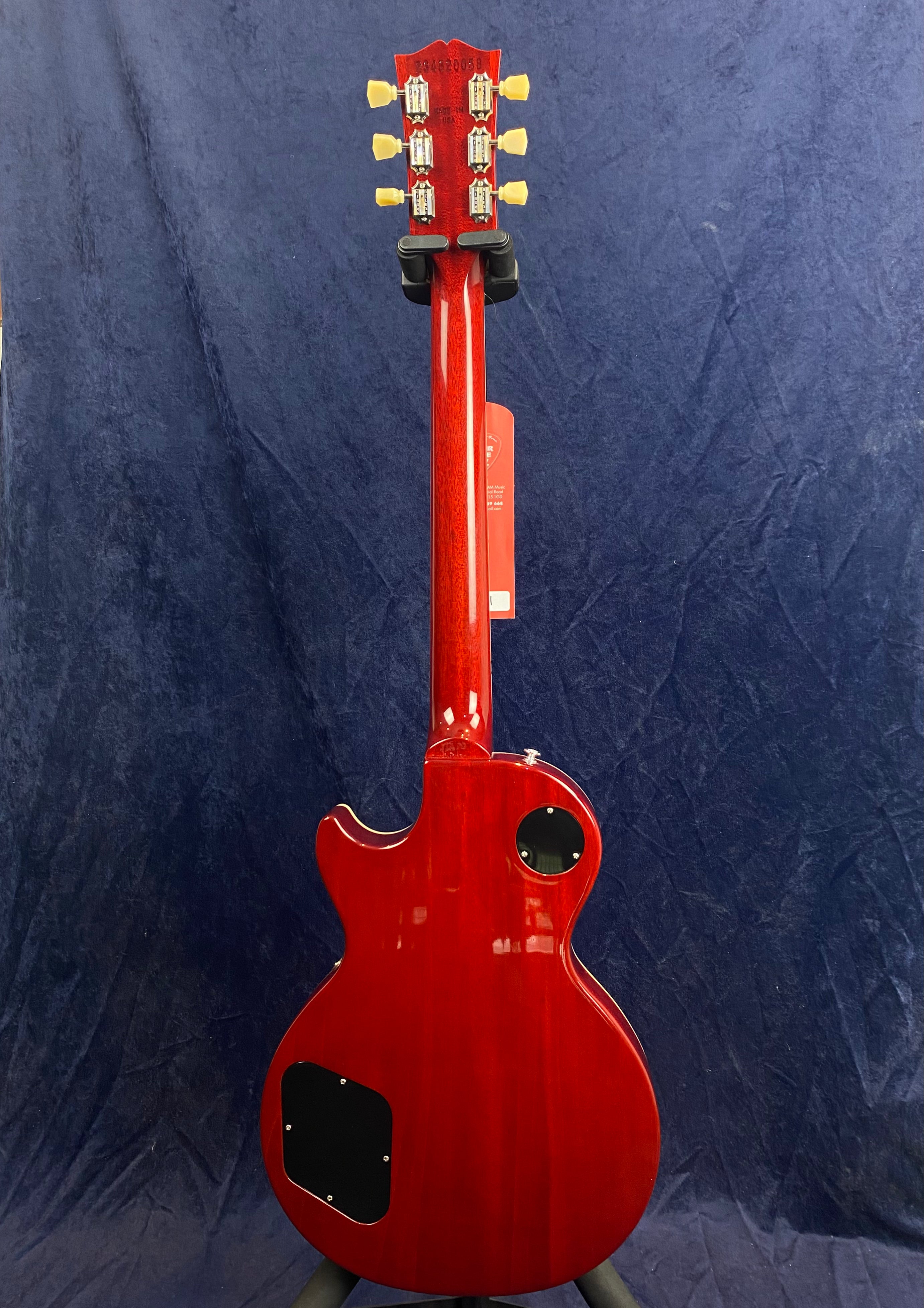 Red electric guitar shown from the back, single-cutaway body, two black electronics covers, cream tuning pegs, set against a dark blue background.